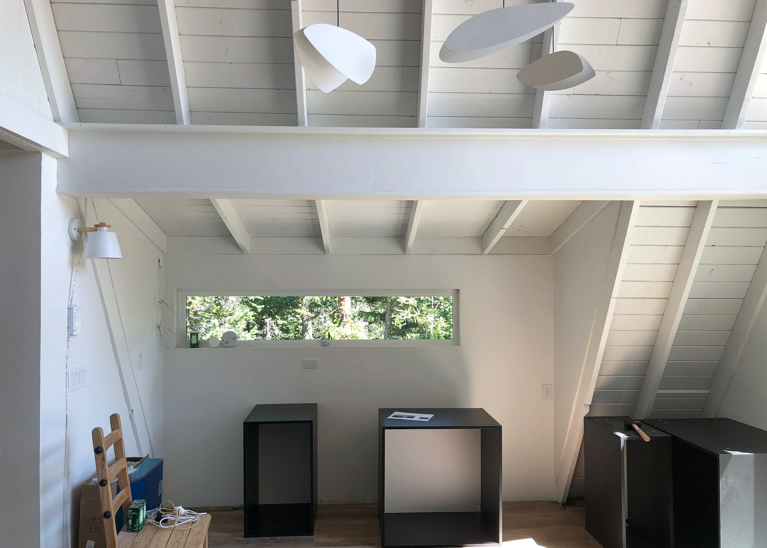 A-frame interior under renovation with white beams and kitchen appliances.