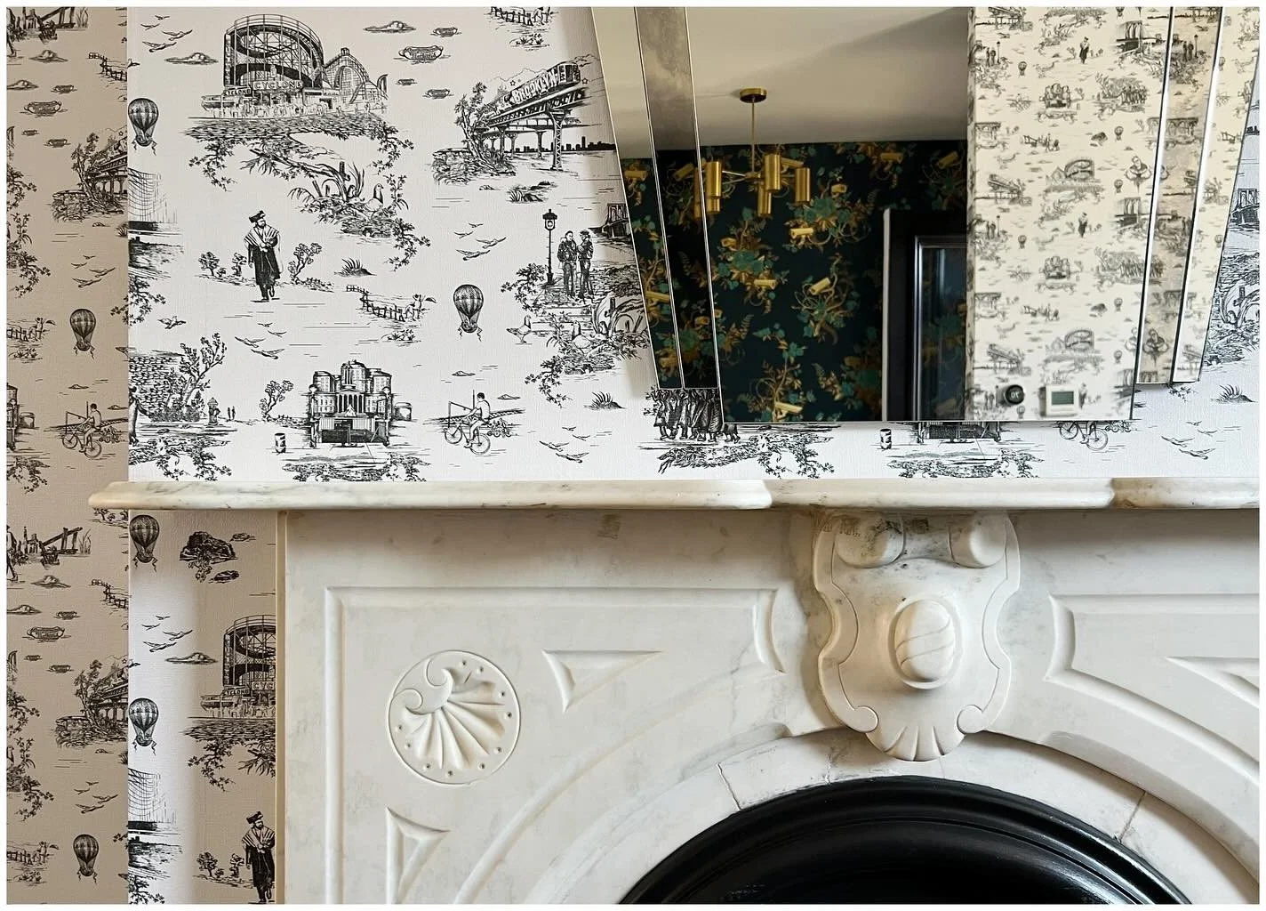 Ornate white fireplace beneath a mirror and botanical wallpaper