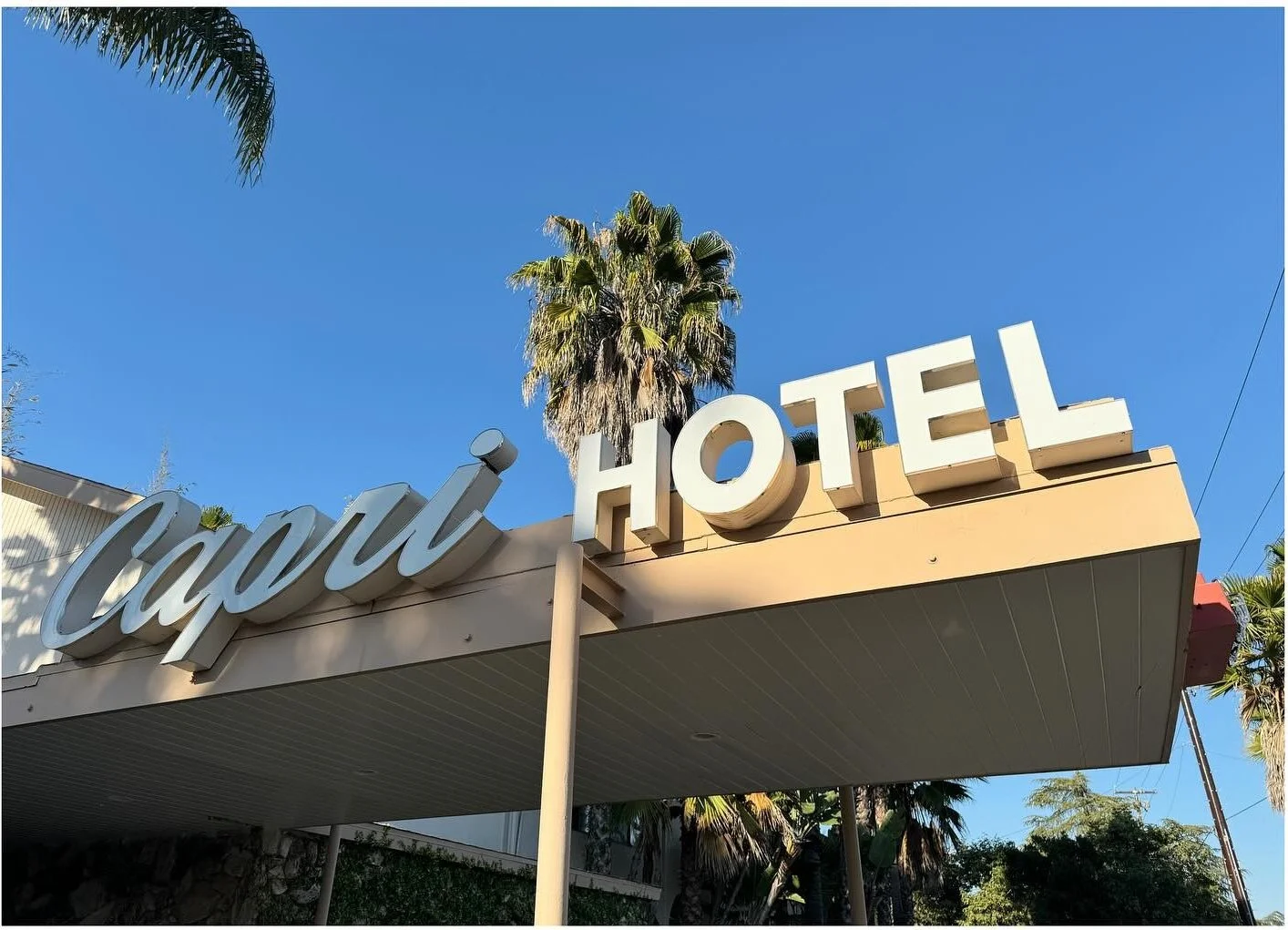 Vintage Capri Hotel sign framed by palm trees against blue sky