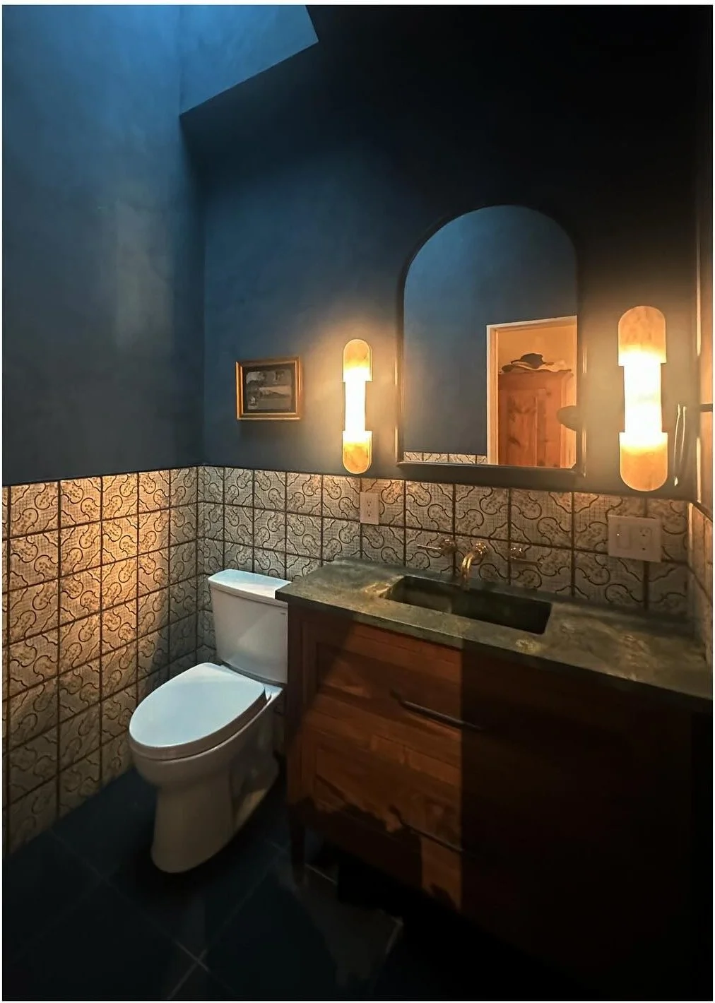 Deep blue bathroom with patterned tile wood vanity and brass fittings