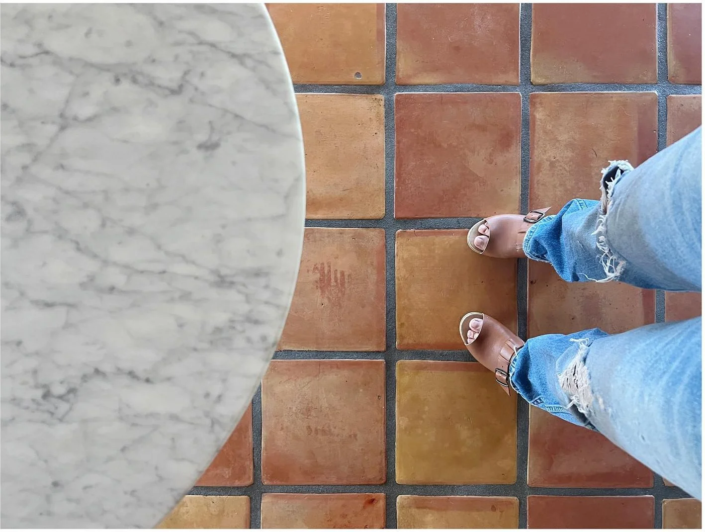 Curved edge of a pale marble table beside terracotta floor tiles