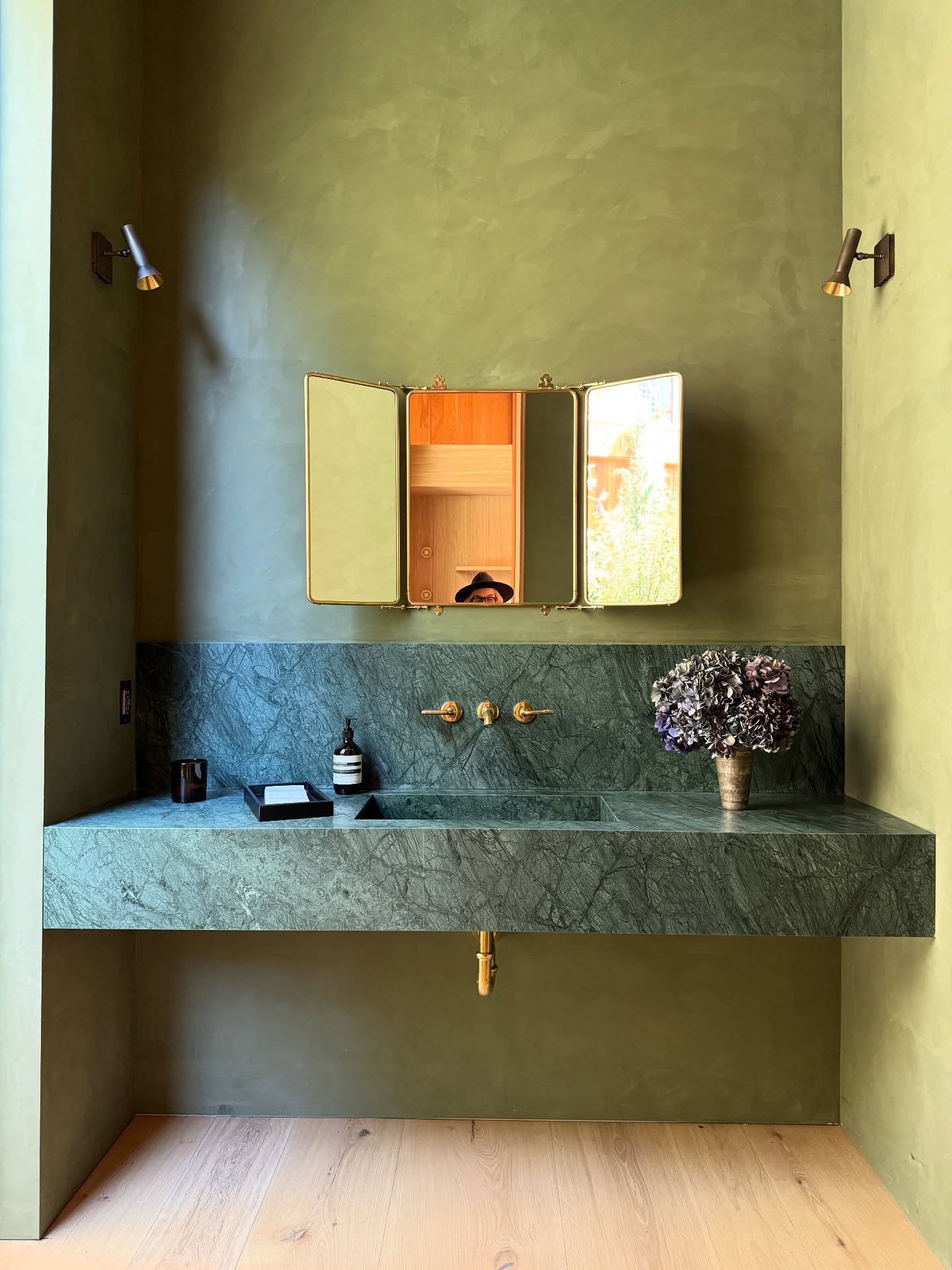Green stone sink beneath gold mirror panels in a green bathroom