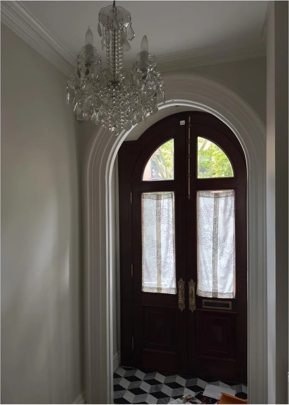 Arched dark wood entry door beneath an ornate crystal chandelier