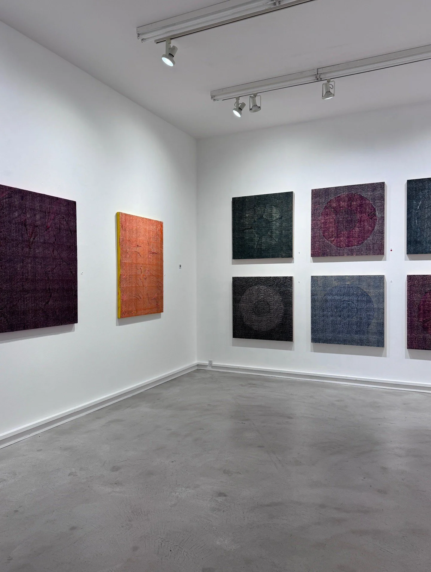 White gallery with colorful square paintings and track lighting