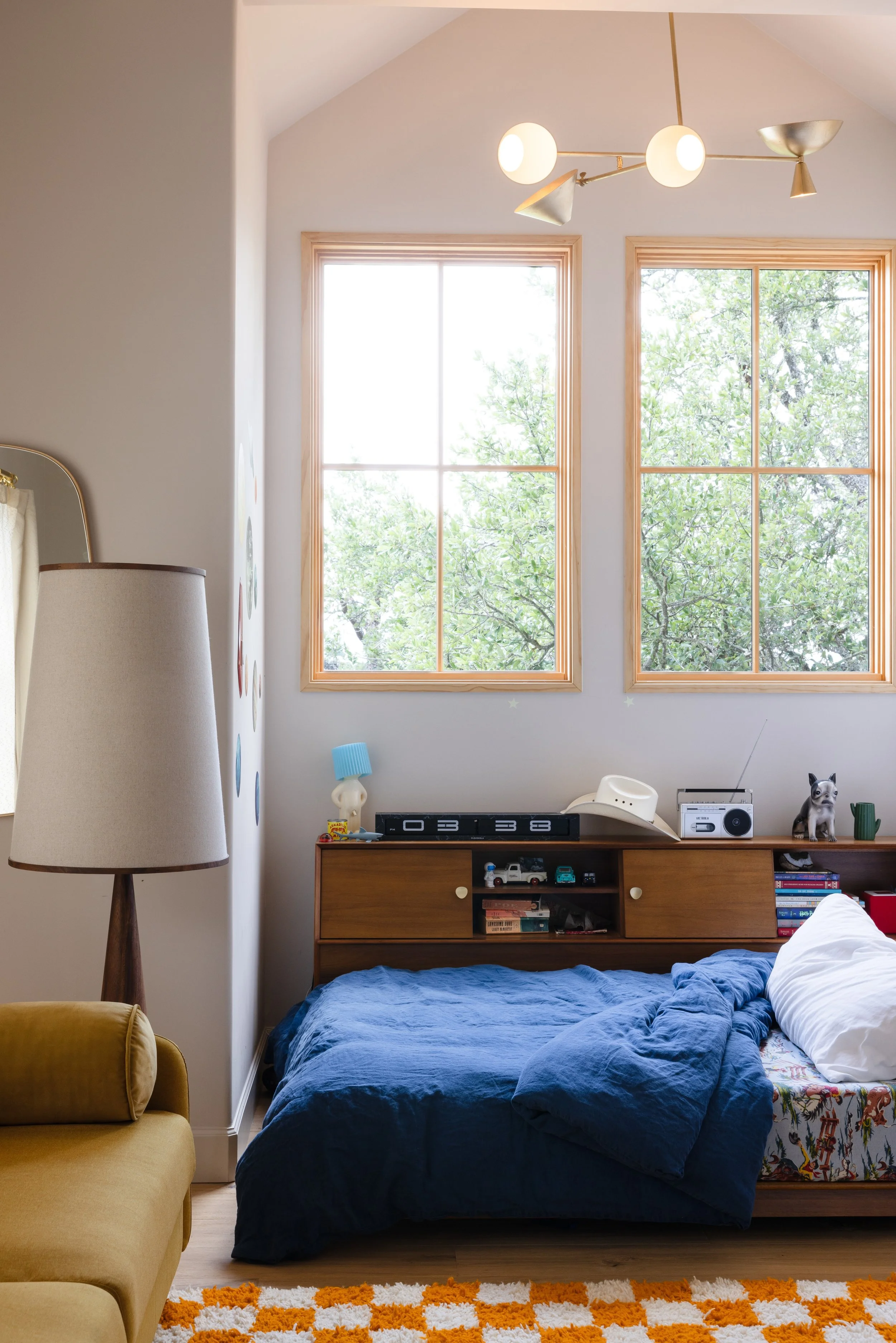 Child’s bedroom with blue bedding, a wood dresser, and orange patterned rug.