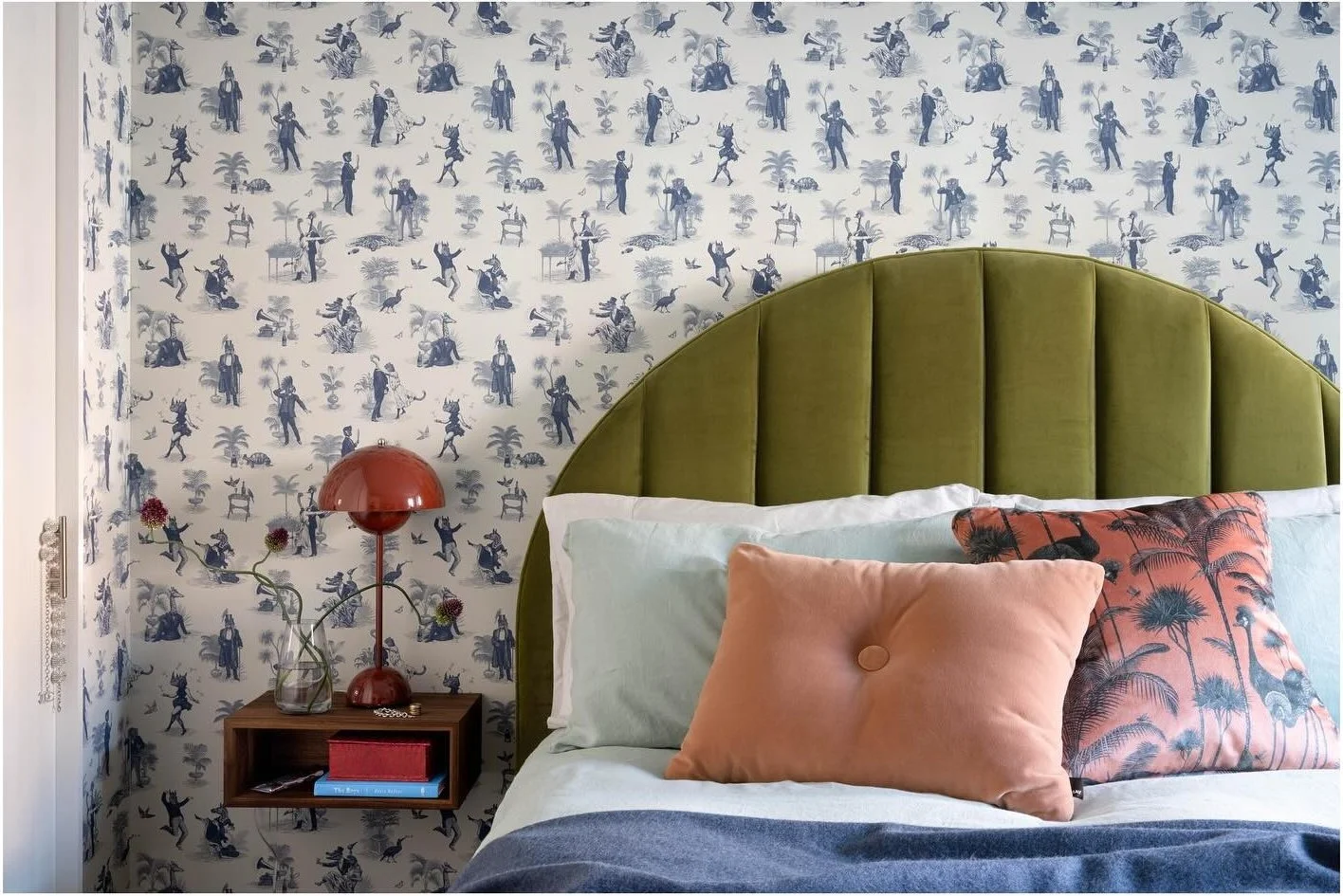 Green velvet headboard against patterned floral wallpaper