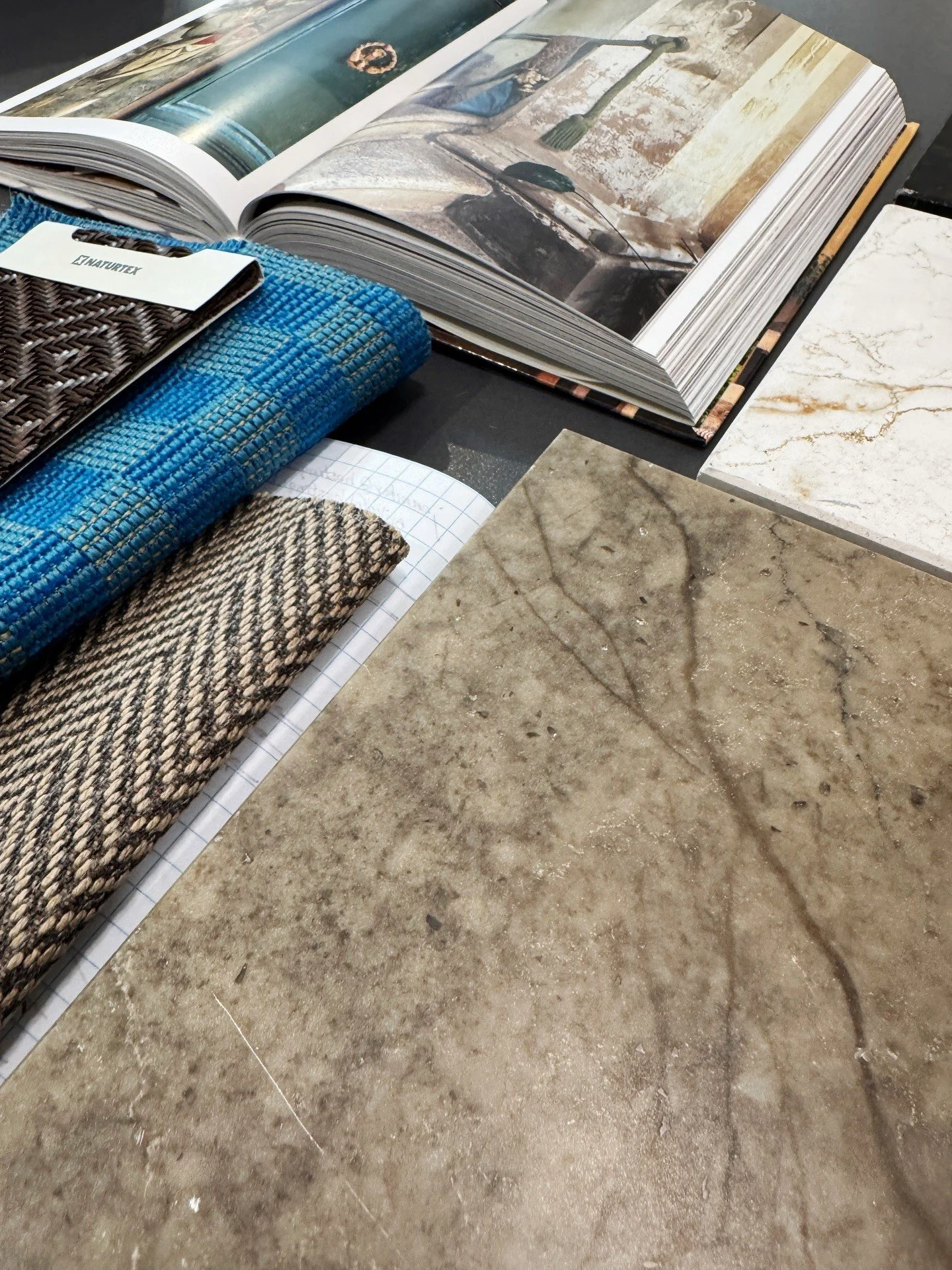 Fabric samples and an open design book beside a veined stone slab