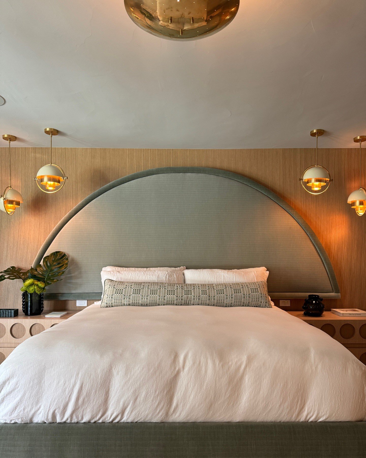 Bedroom with a curved green headboard and brass wall lights
