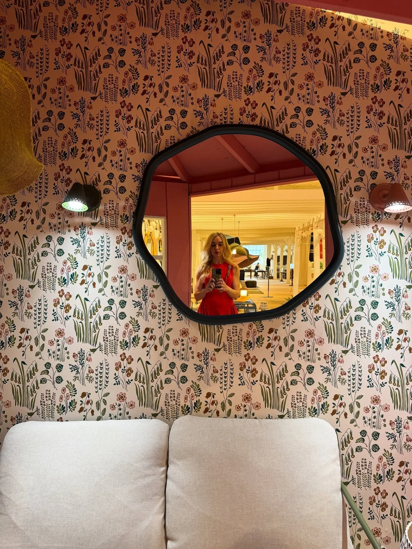 Patterned wallpaper and round mirror above a pale sofa