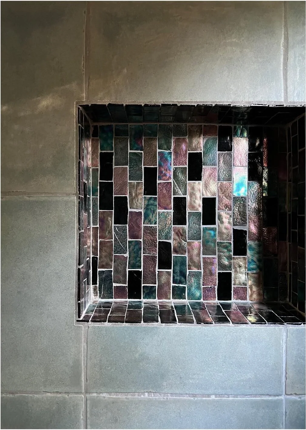 Recessed shower niche framed by gray tile and multicolored mosaic