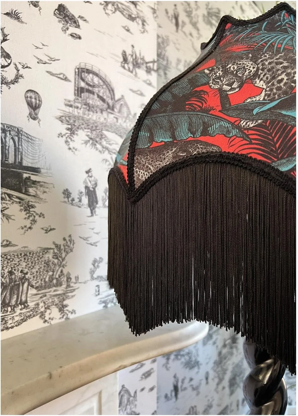 Fringed red and black lampshade against illustrated wallpaper