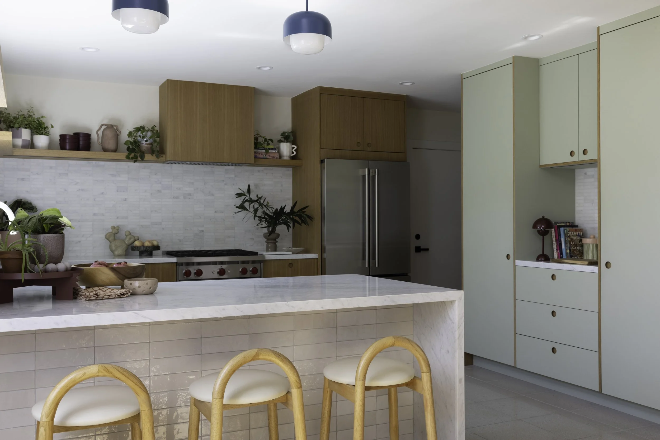 Kitchen with wood and sage cabinetry, a white island, and yellow stools.