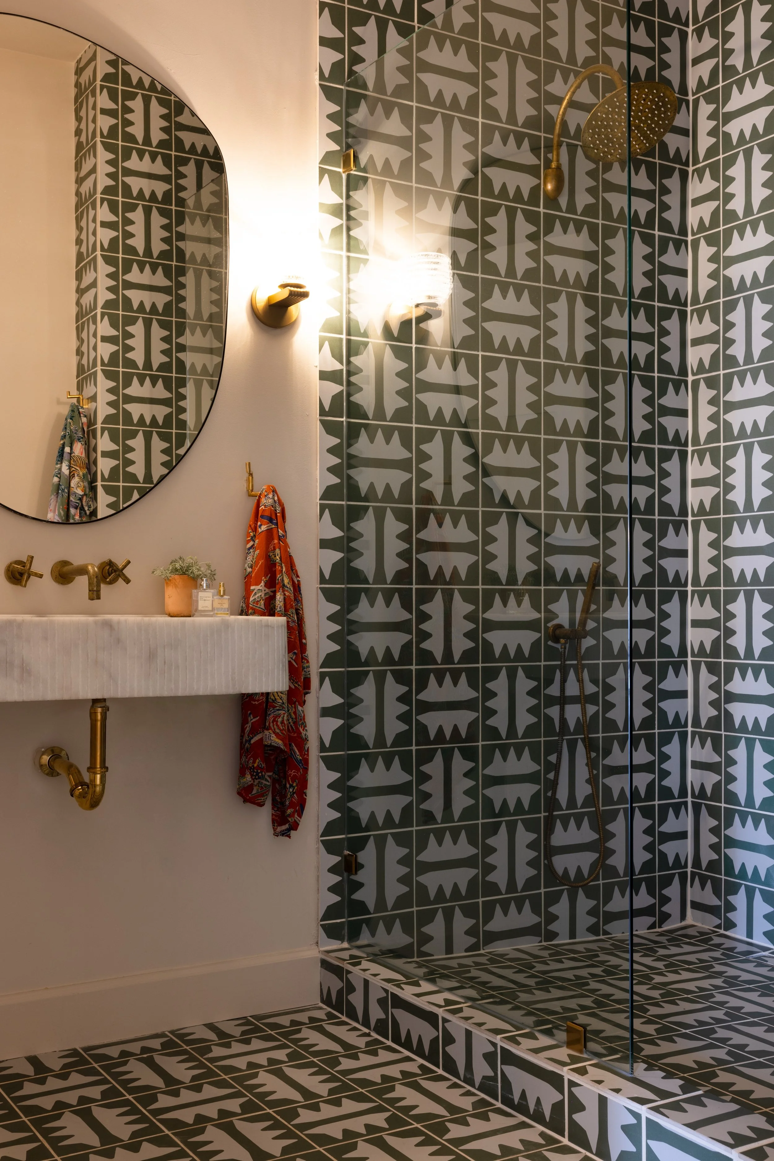Bathroom with patterned tile shower, stone sink, and brass fixtures.