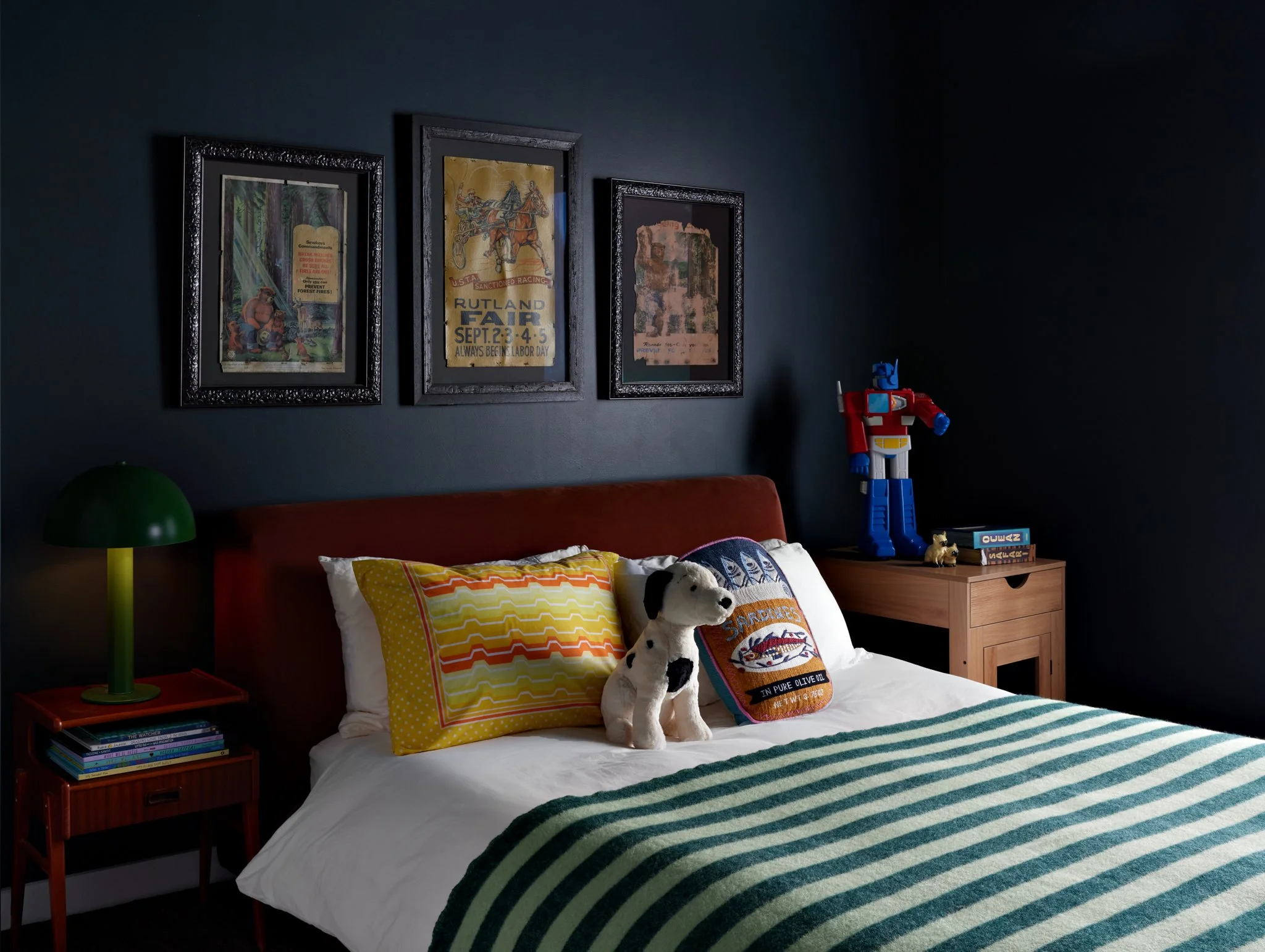 Dark blue bedroom with a red headboard, striped bedding, and framed art.