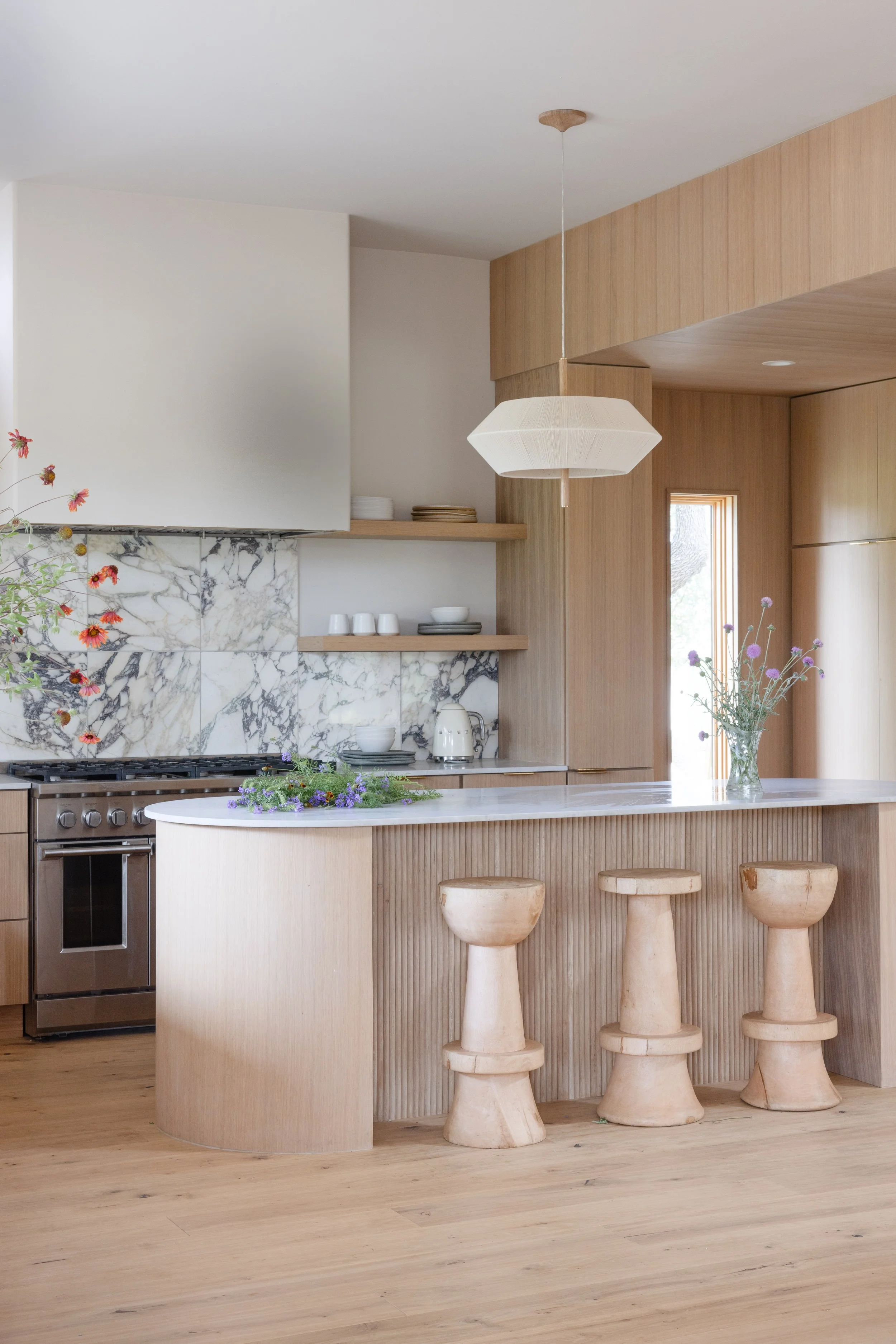 Light wood kitchen with a curved island and sculptural stools.