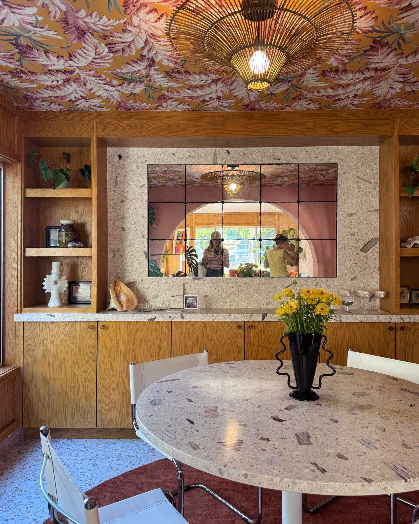 Round terrazzo dining table beneath floral wallpaper ceiling