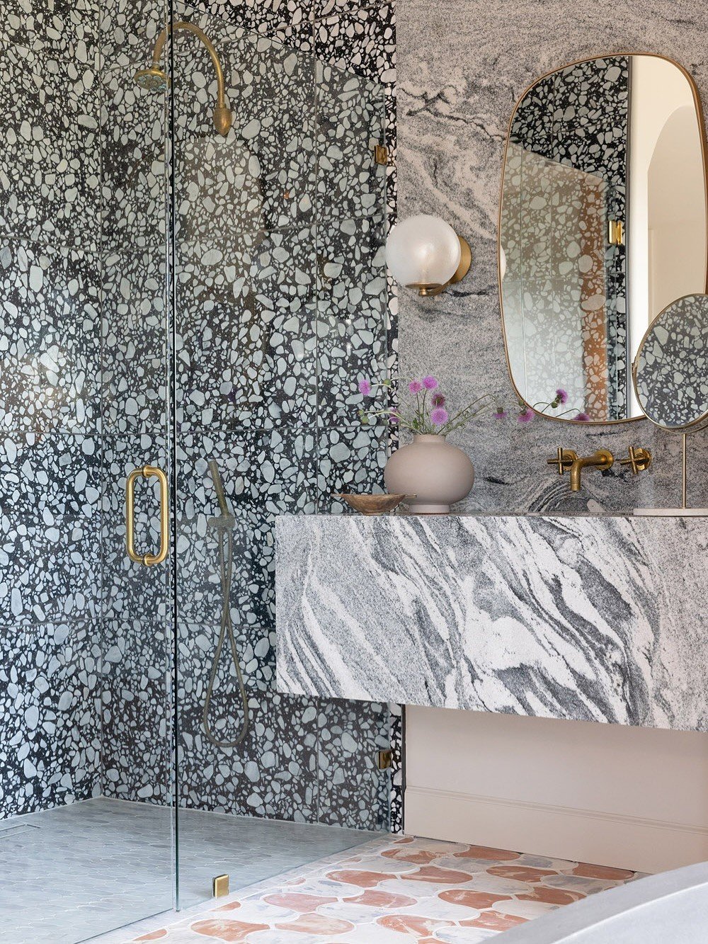 Terrazzo shower and veined stone vanity with brass fixtures