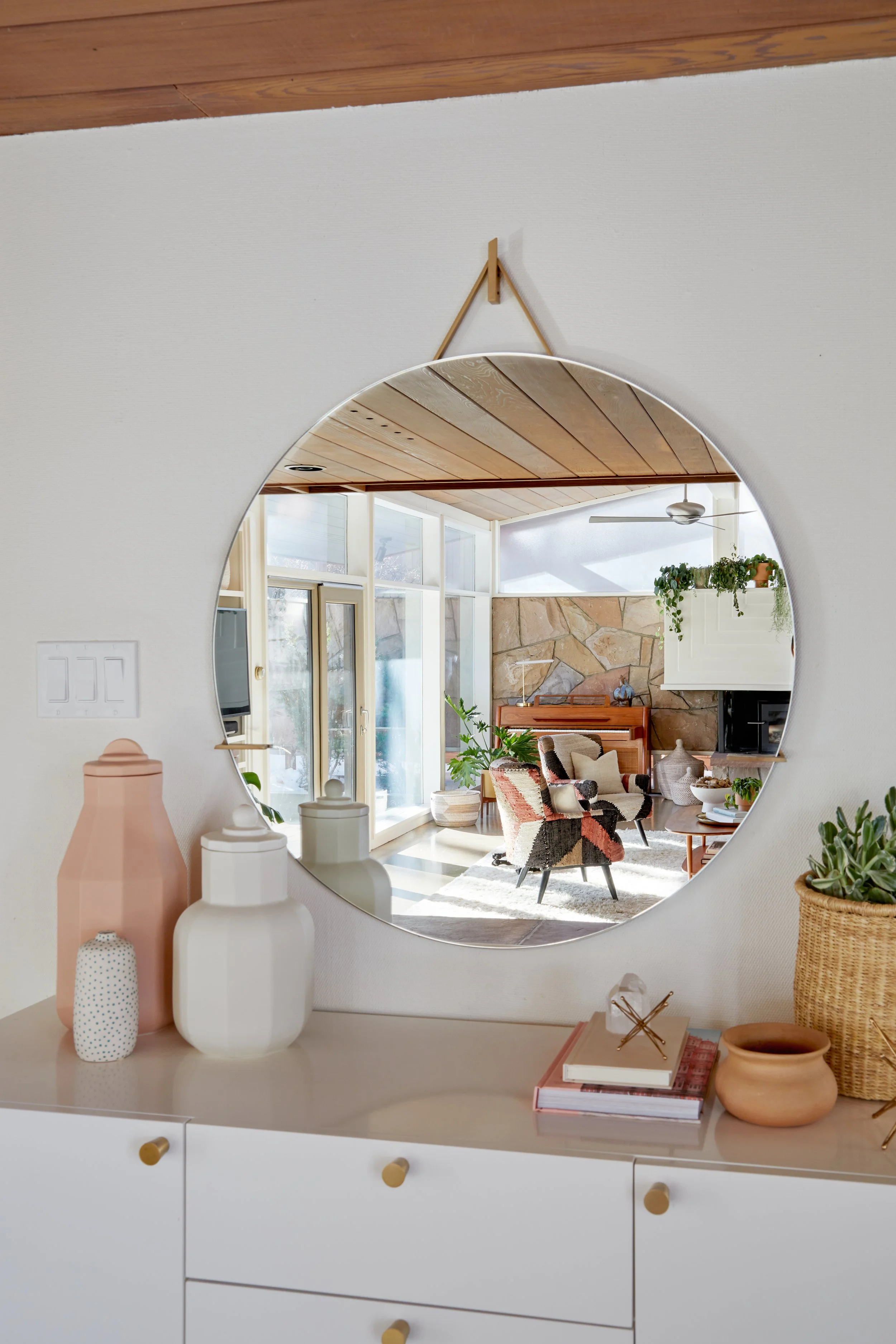Round mirror above a white dresser reflecting a dining area.