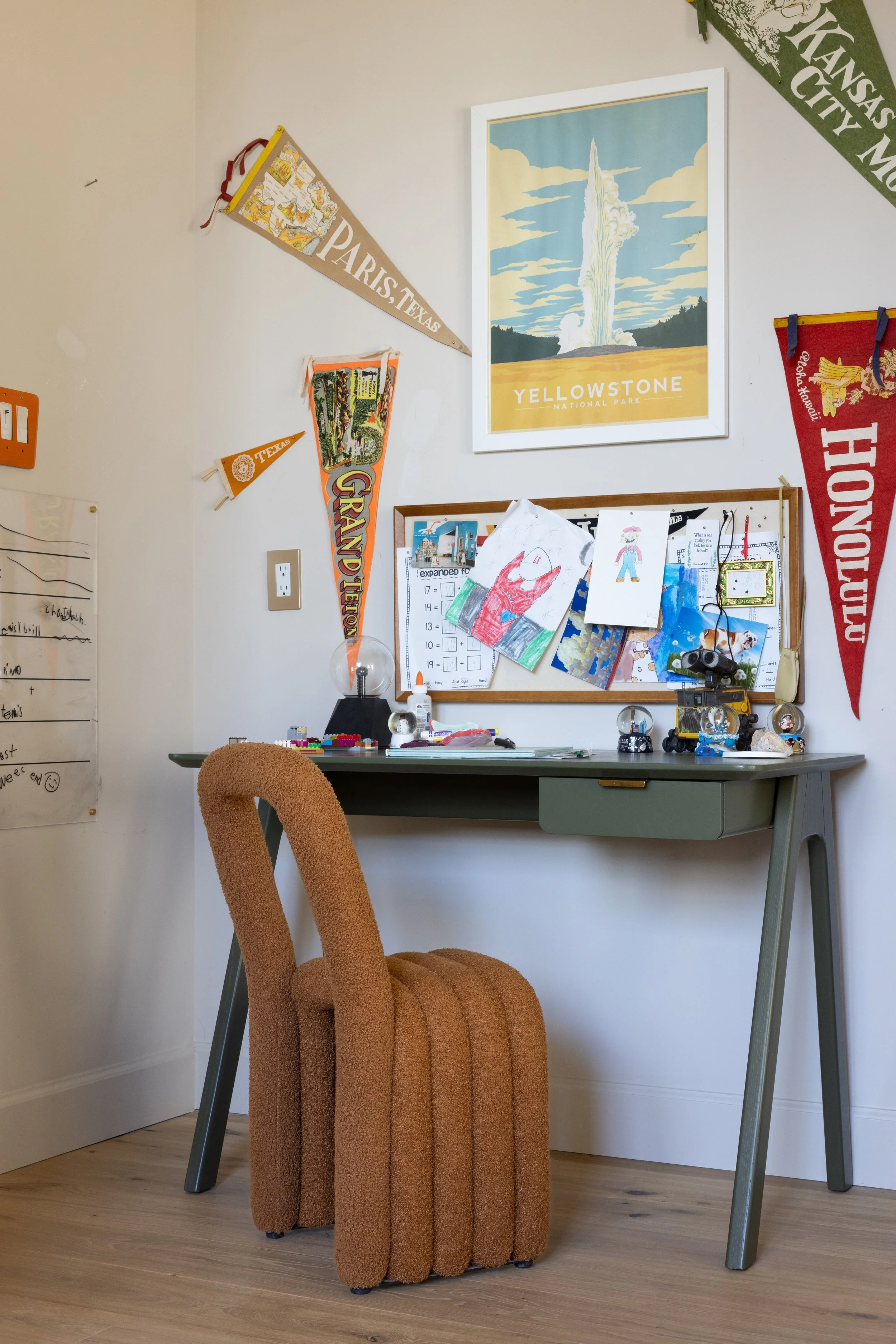 Child’s desk with artwork, pennants, and a sculptural brown chair.