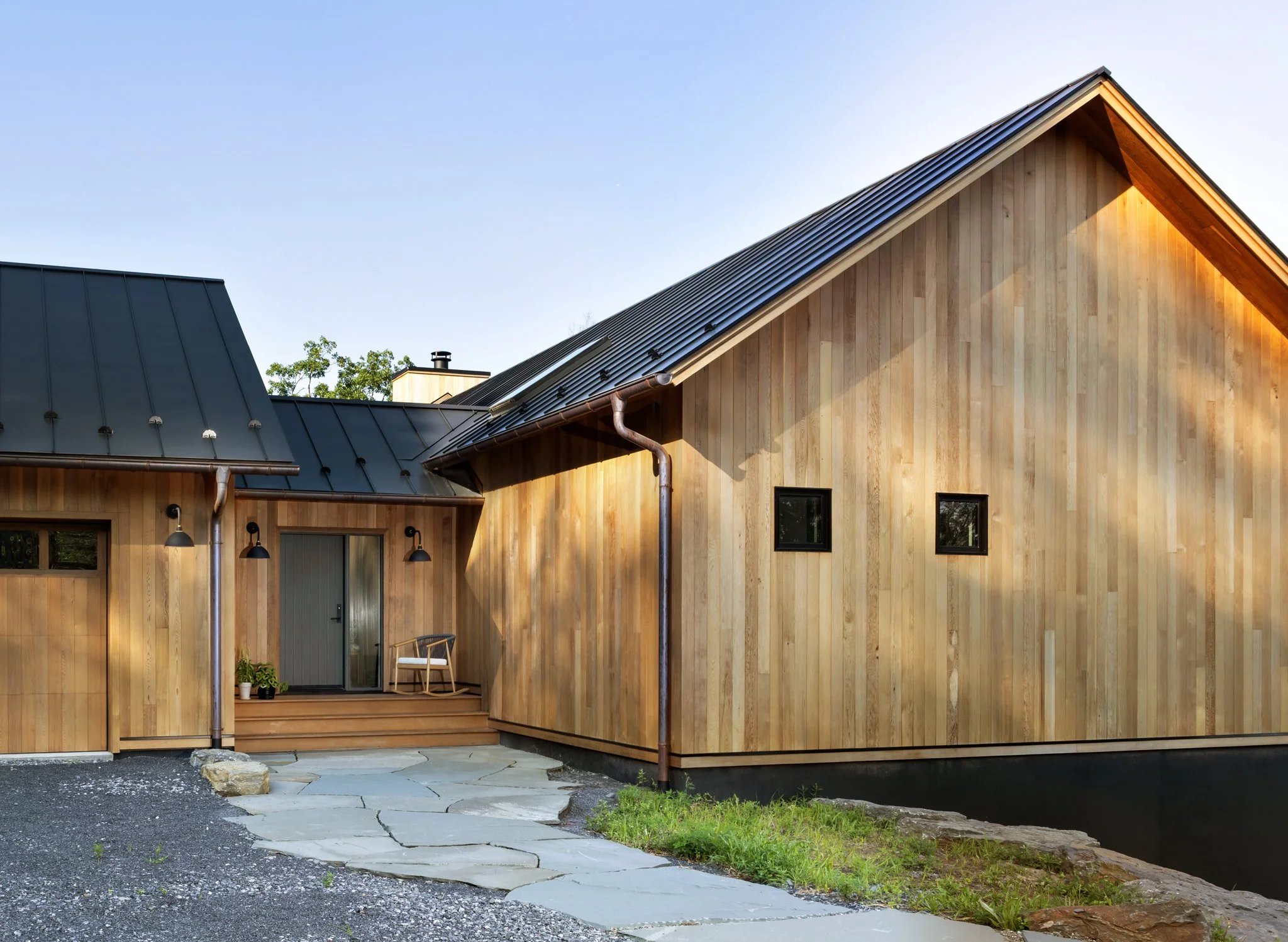 Exterior of a wood-clad home with dark metal roof and stone walkway.