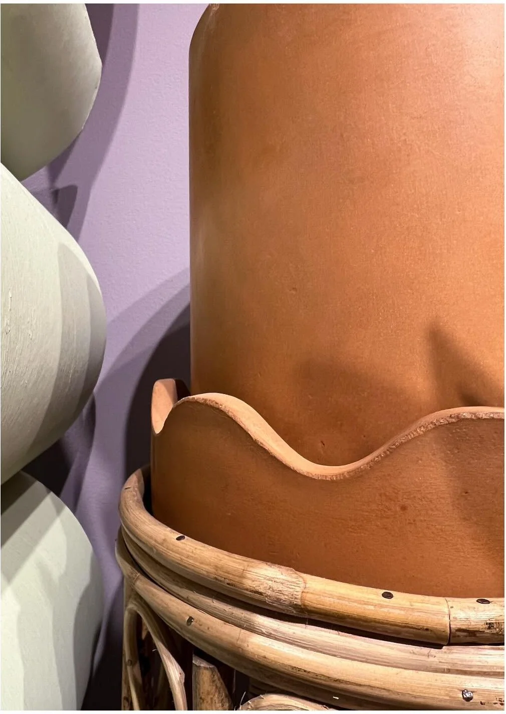 Terracotta planter with a wavy rim beside rounded pale pots