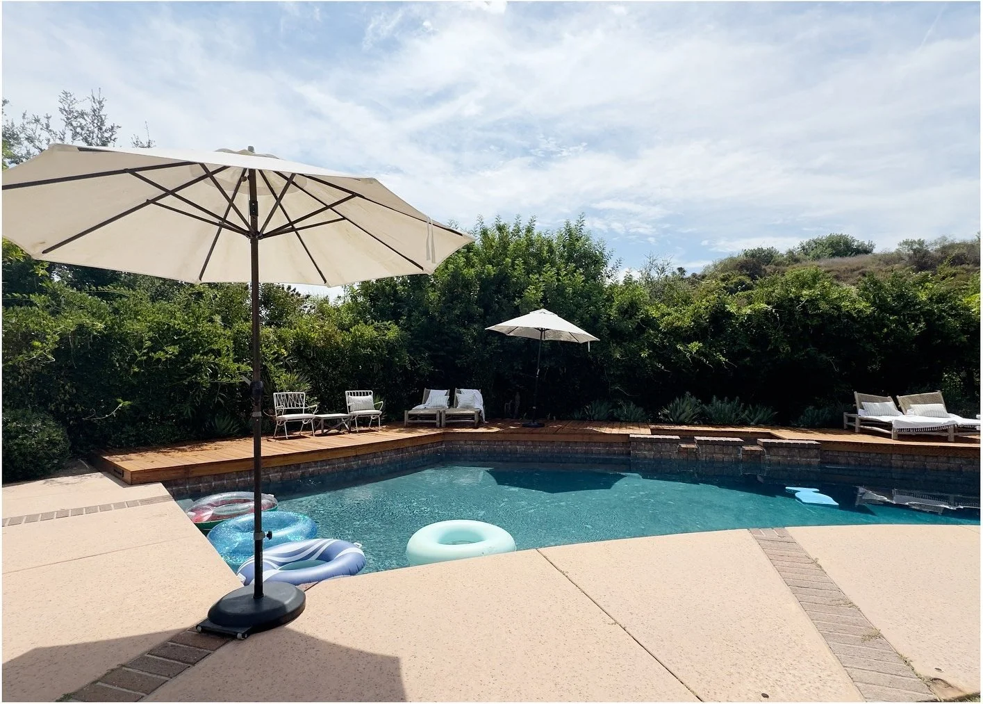 Pool terrace with pale umbrellas and mature green hedges