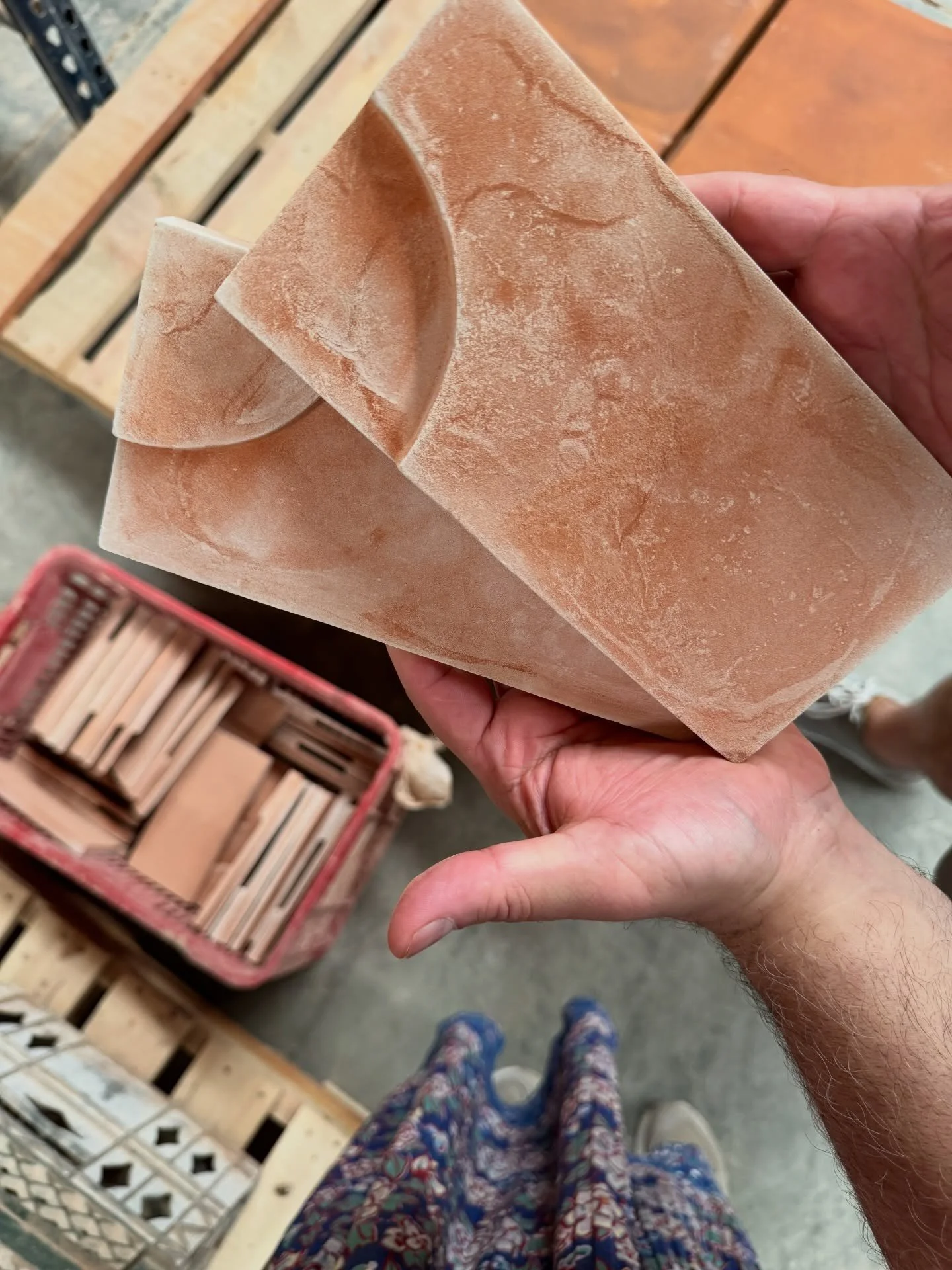 Hand holding a warm terracotta tile beside stacked samples