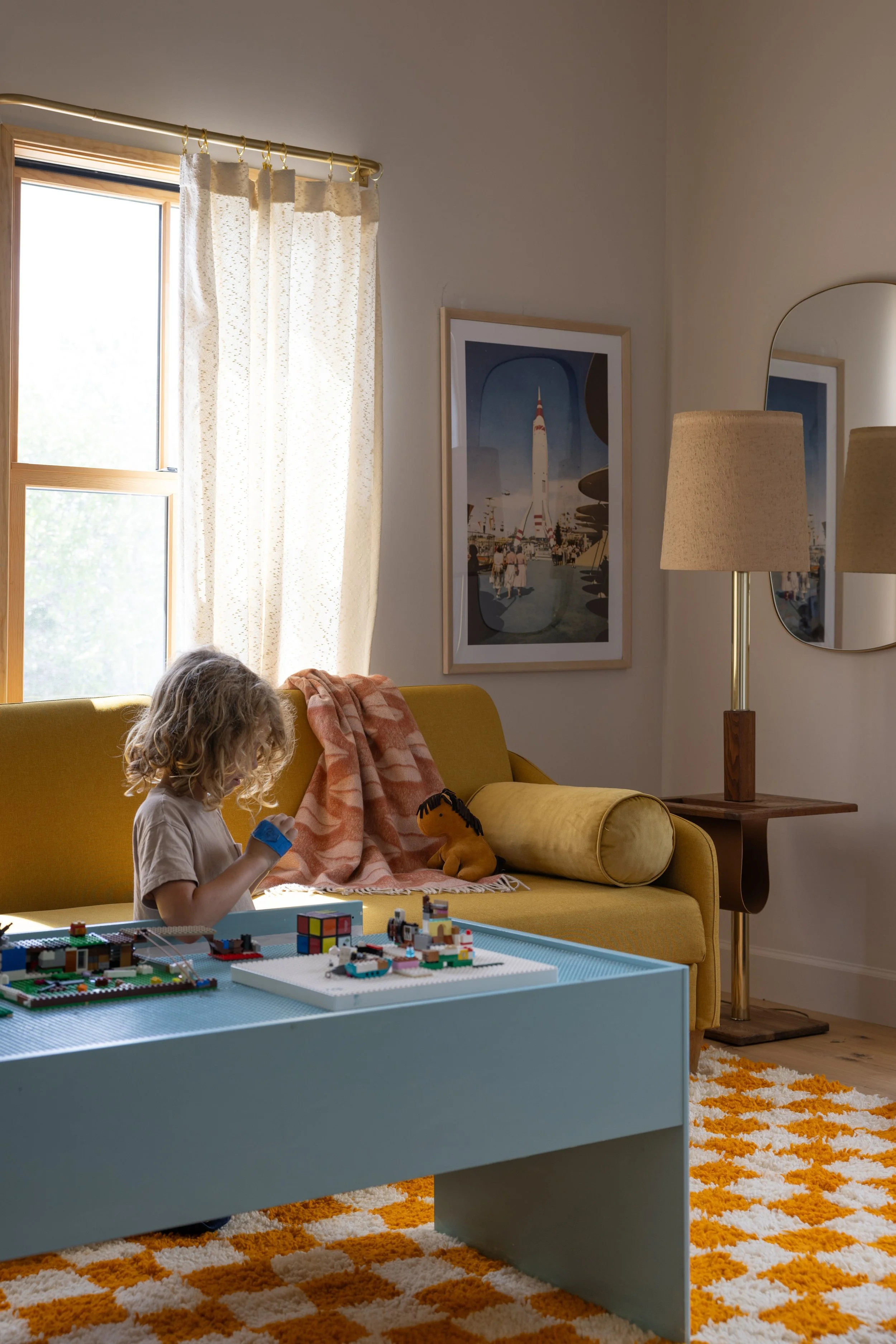 Child seated at a play table beside a mustard sofa and patterned rug.
