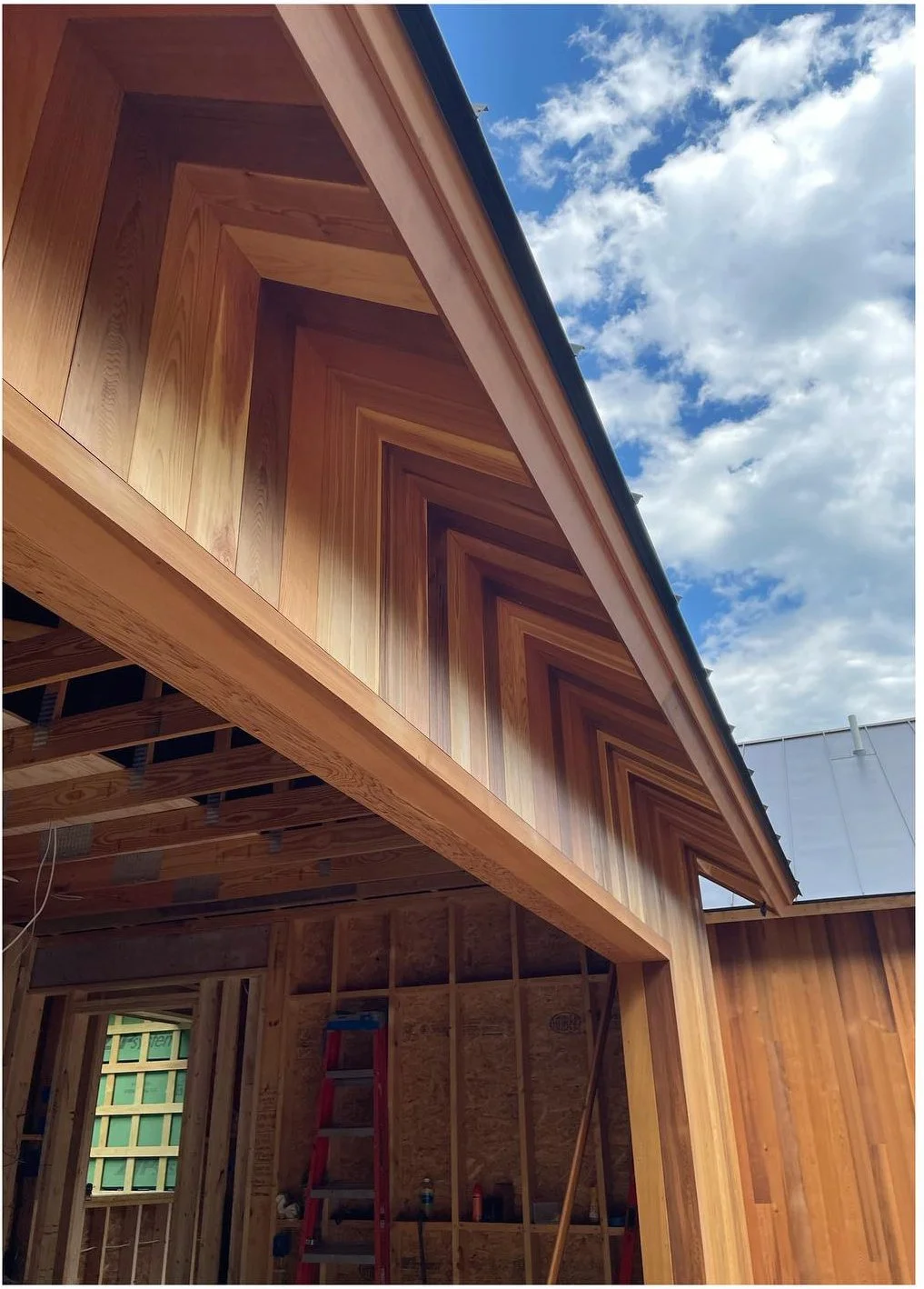 Timber roof framing and exterior wood cladding beneath a blue sky
