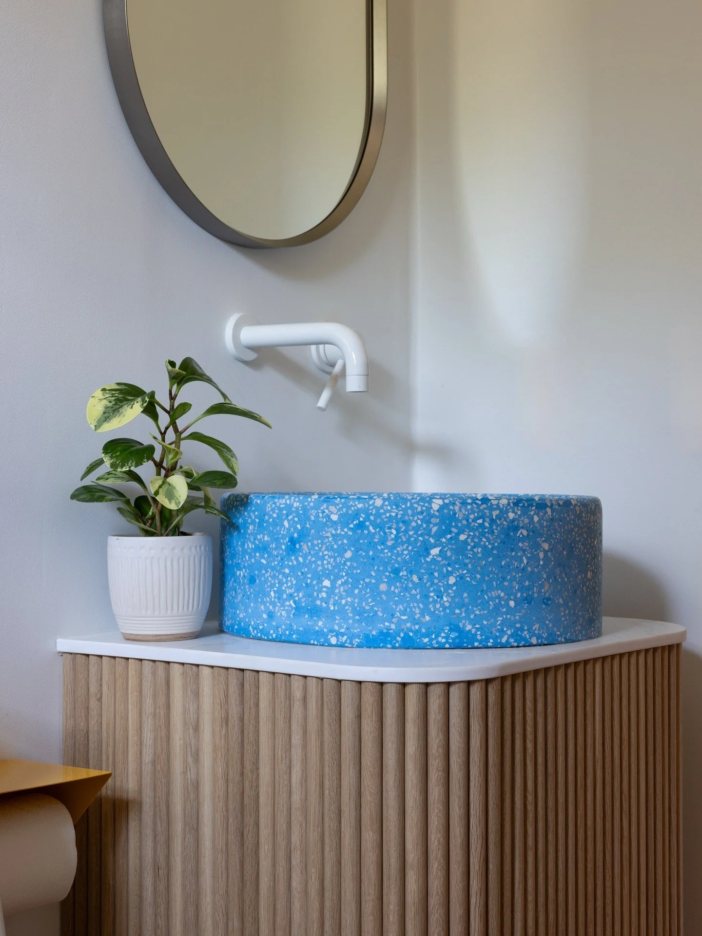 Blue terrazzo basin on a curved oak vanity beside a plant