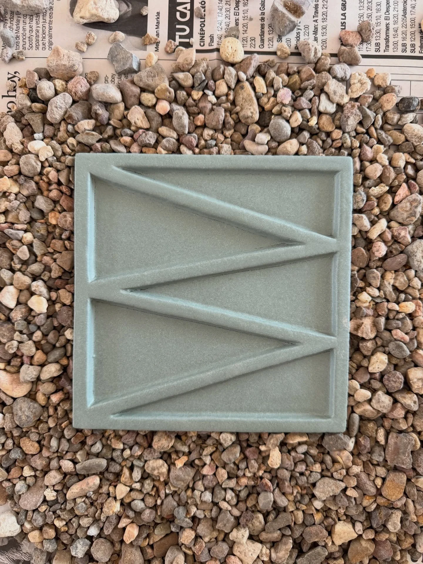 Sage green square tile with raised zigzag relief on gravel