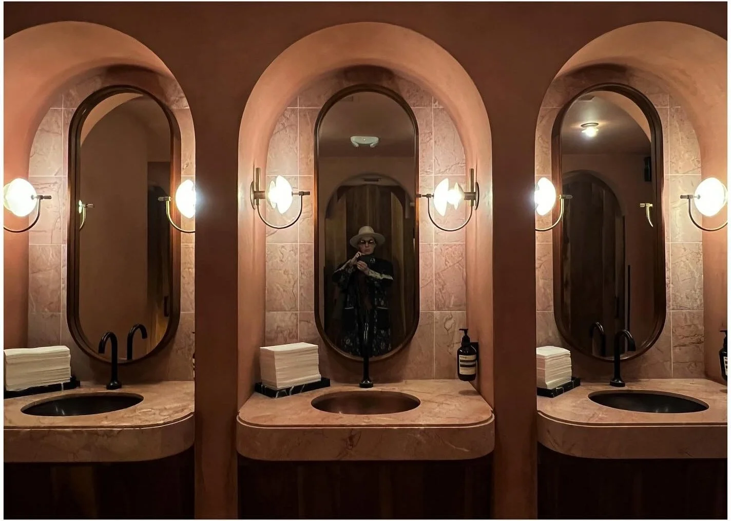 Terracotta bathroom with arched mirrors and warm globe lighting