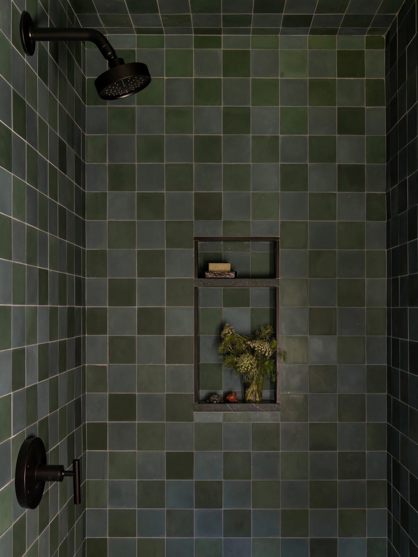 Green tiled shower with dark fixtures and a recessed niche
