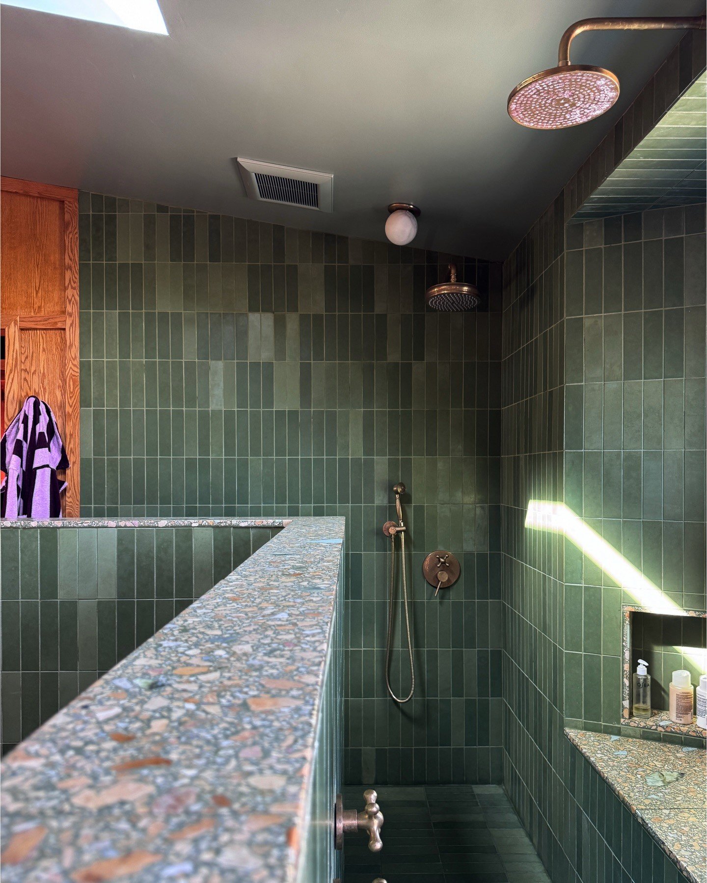 Green tiled shower with a colorful terrazzo partition