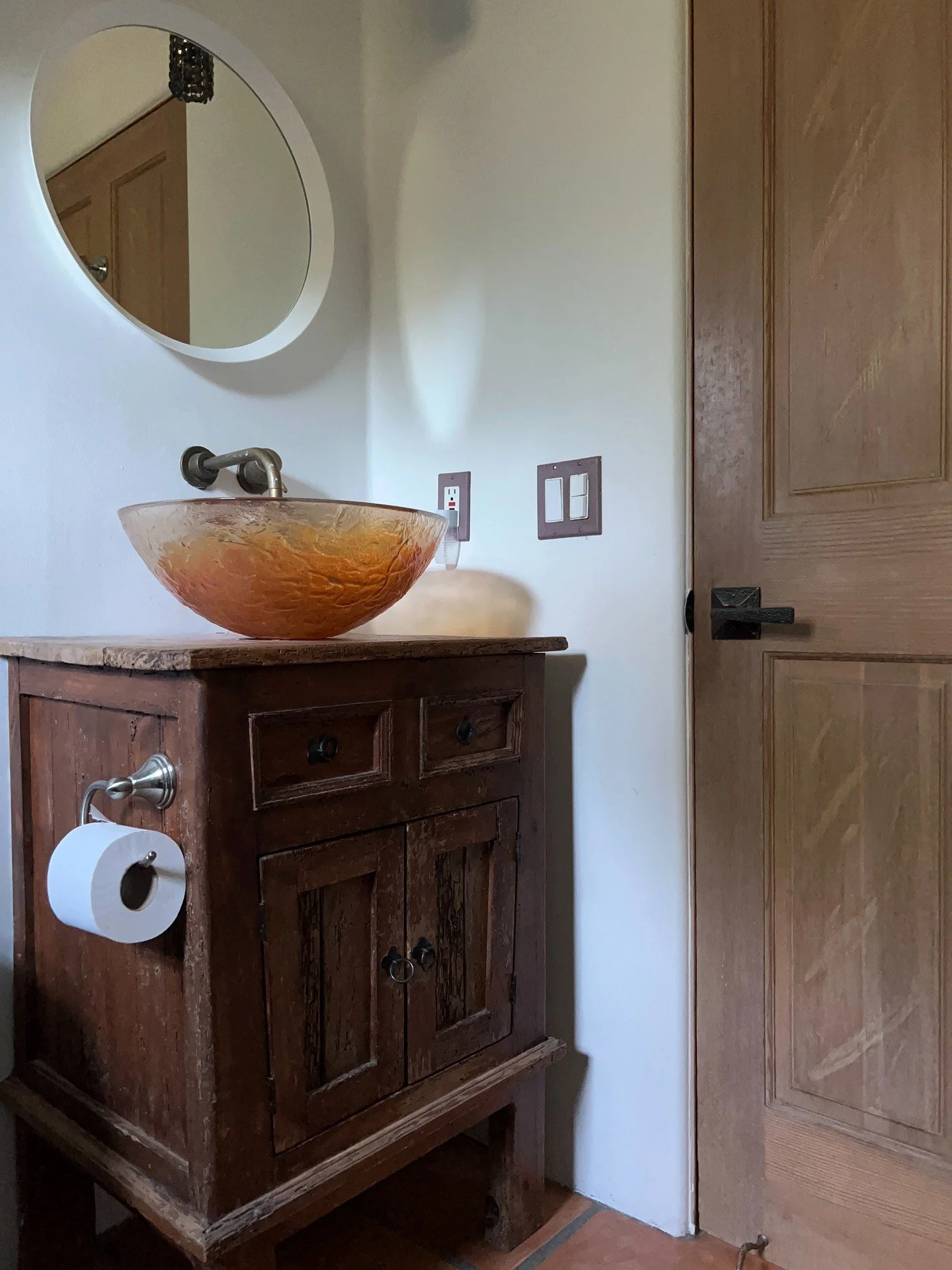 Carved wood vanity with amber basin beneath a round mirror