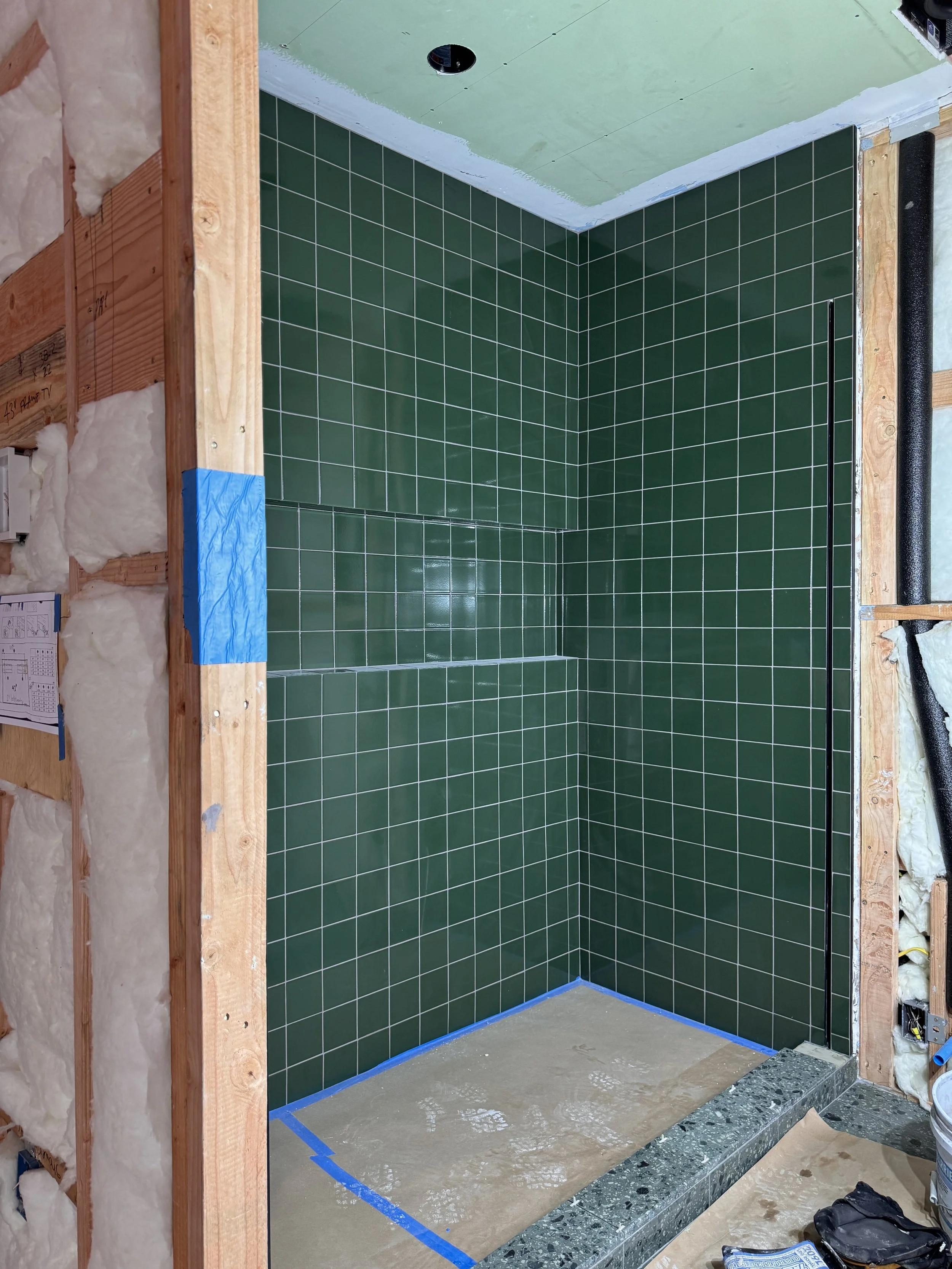 Green tiled shower under construction with exposed framing around the doorway.