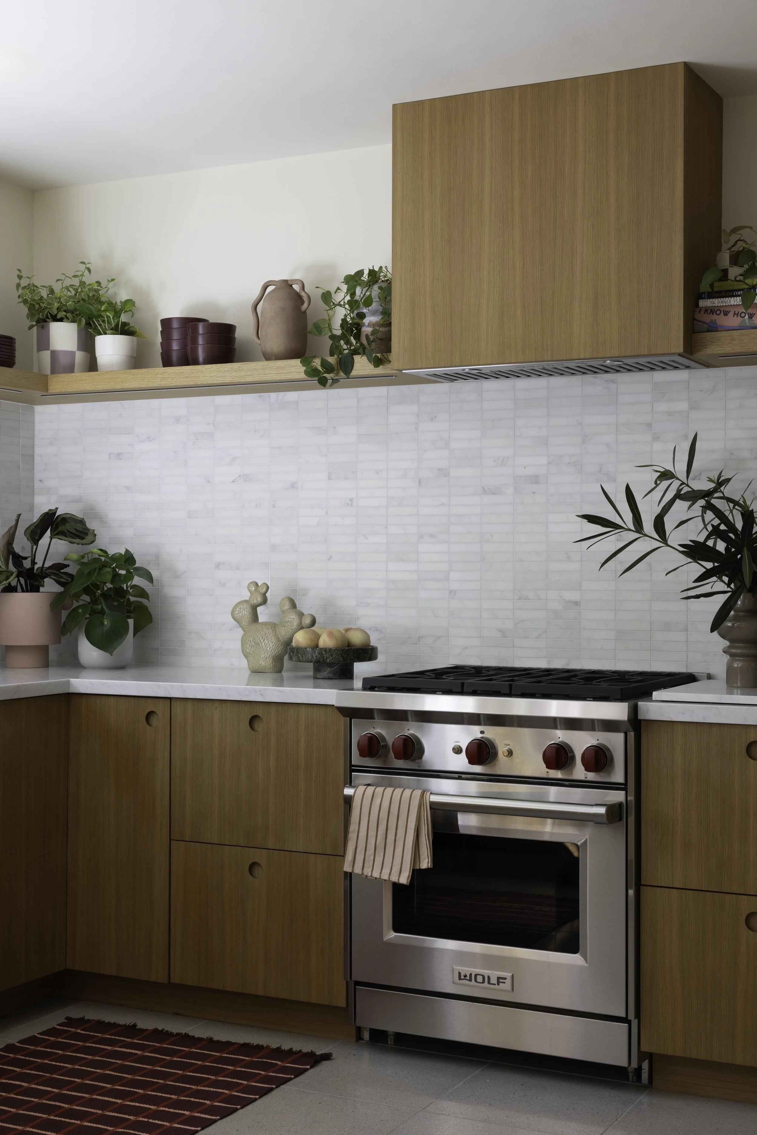Kitchen with wood cabinets, open shelves, white tile, and a stainless range.