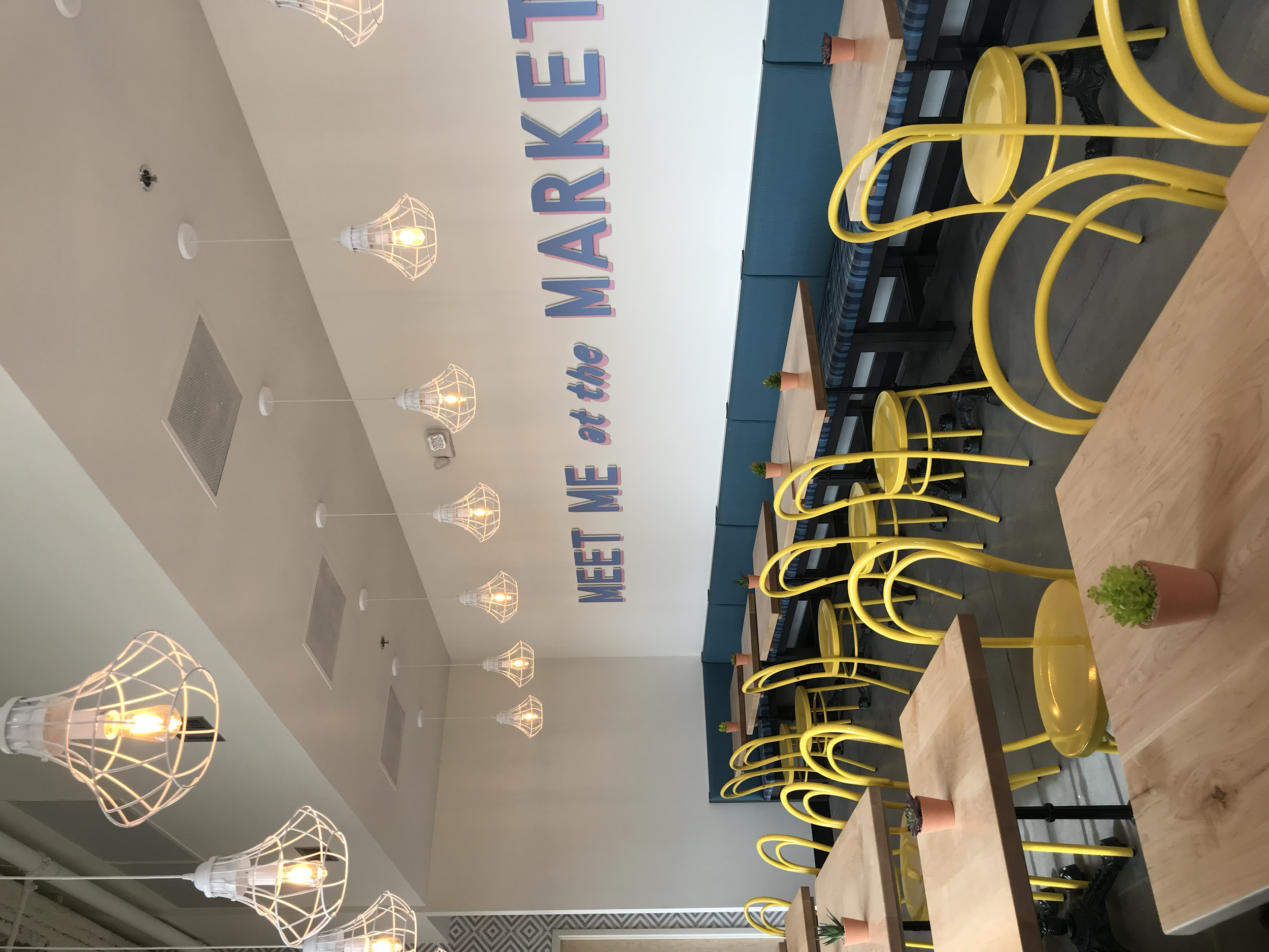 Restaurant dining room with yellow chairs, blue banquettes, and wire pendant lights.