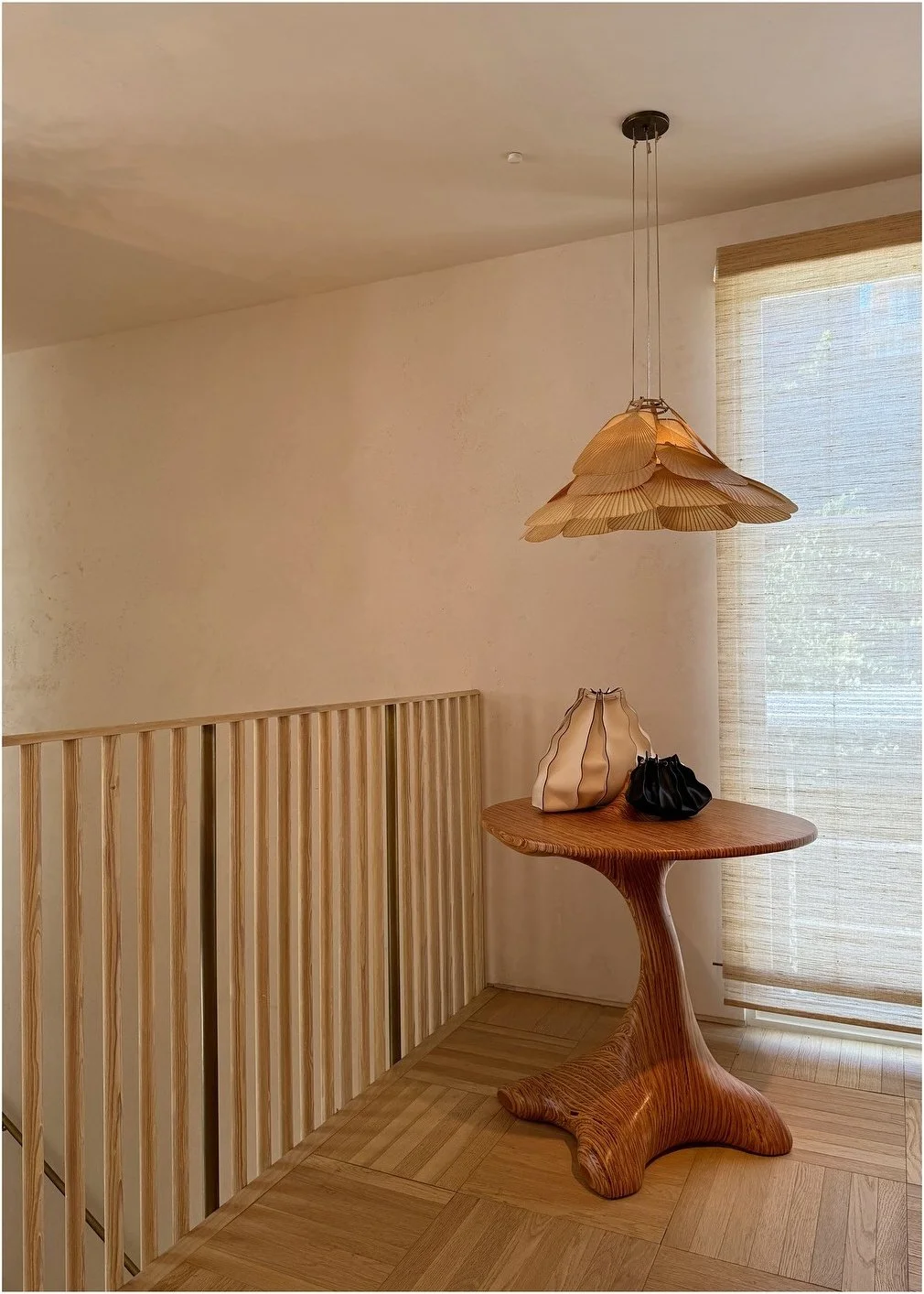 Woven pendant above a small wood table beside a stair railing