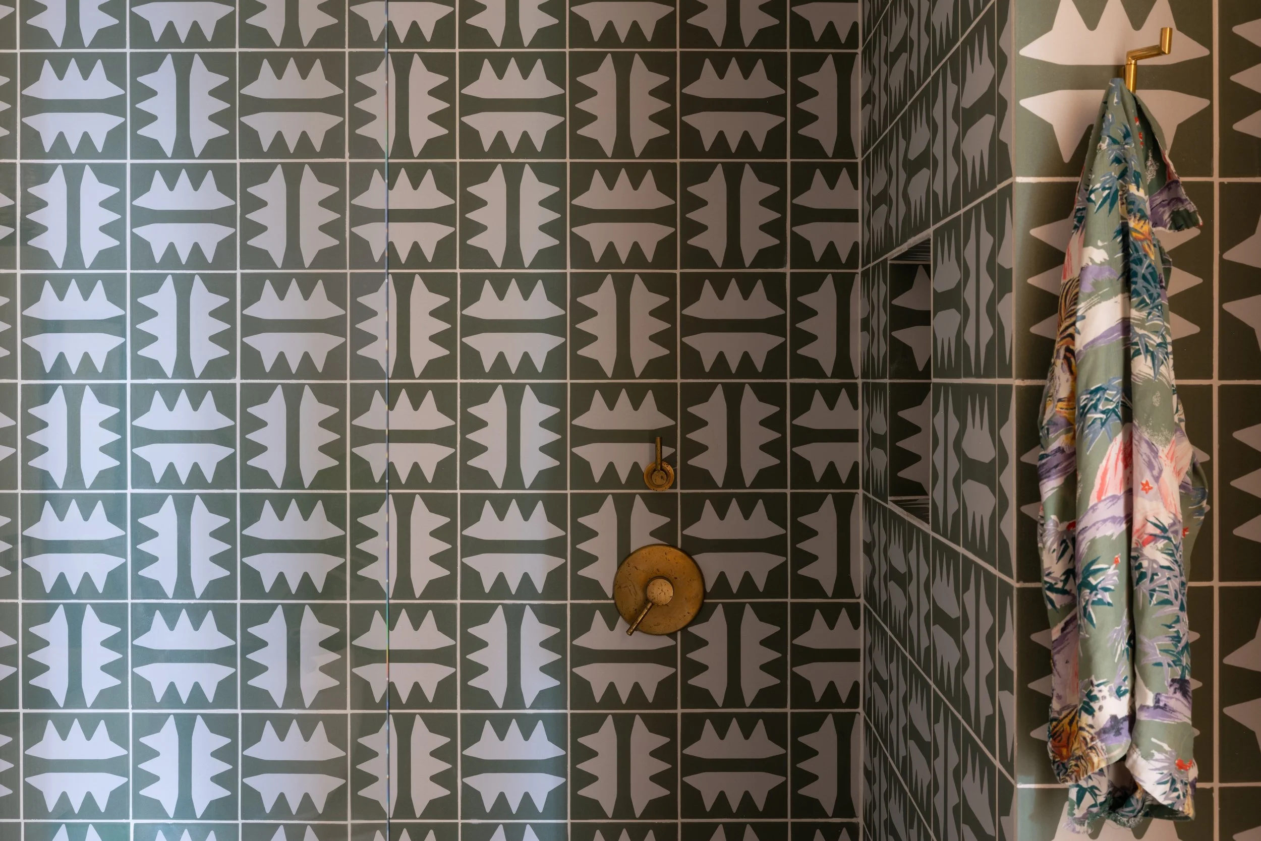 Patterned bathroom tile with brass shower fixtures and a floral robe.