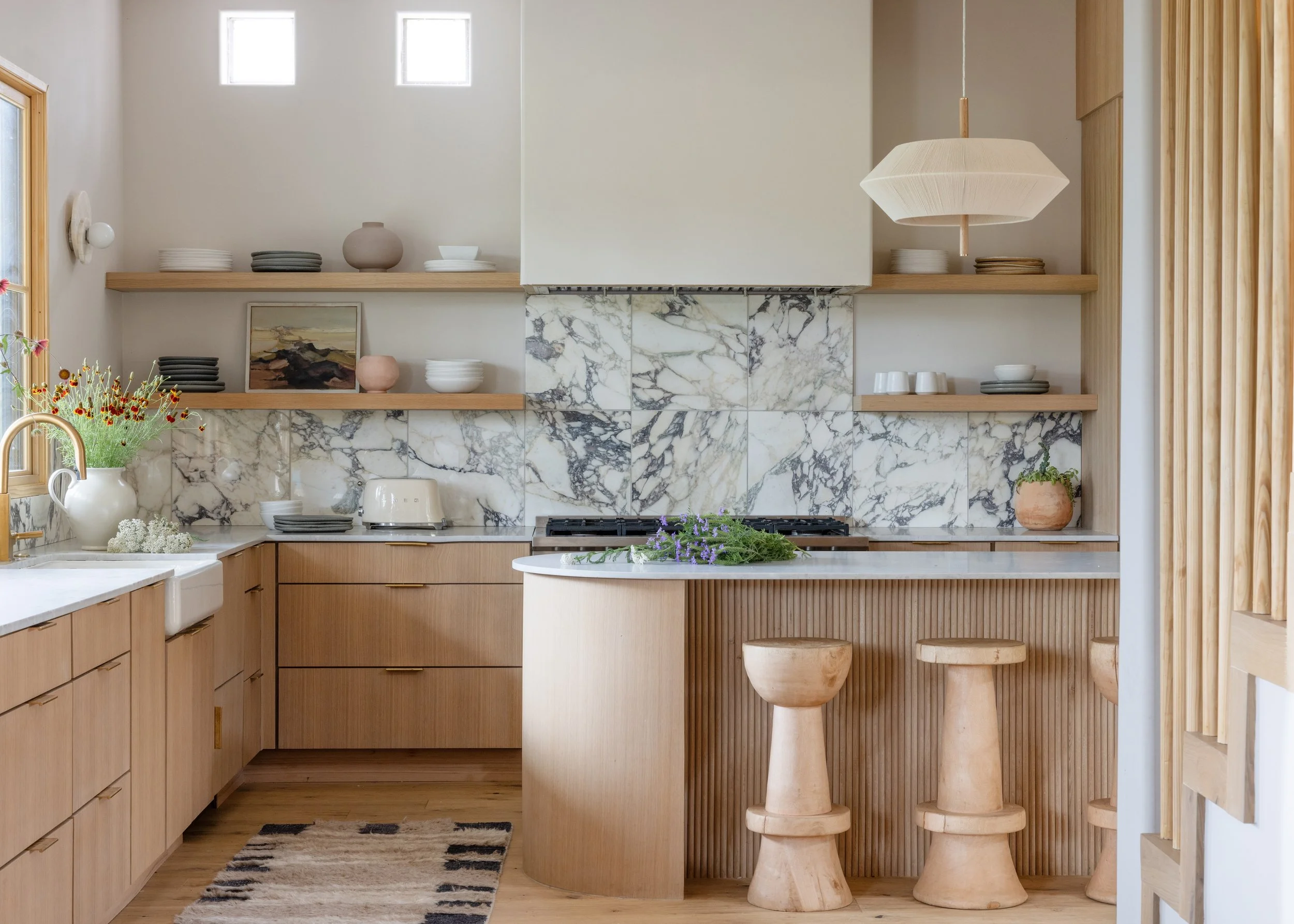 Kitchen with a marble backsplash, curved wood island, and sculptural stools.