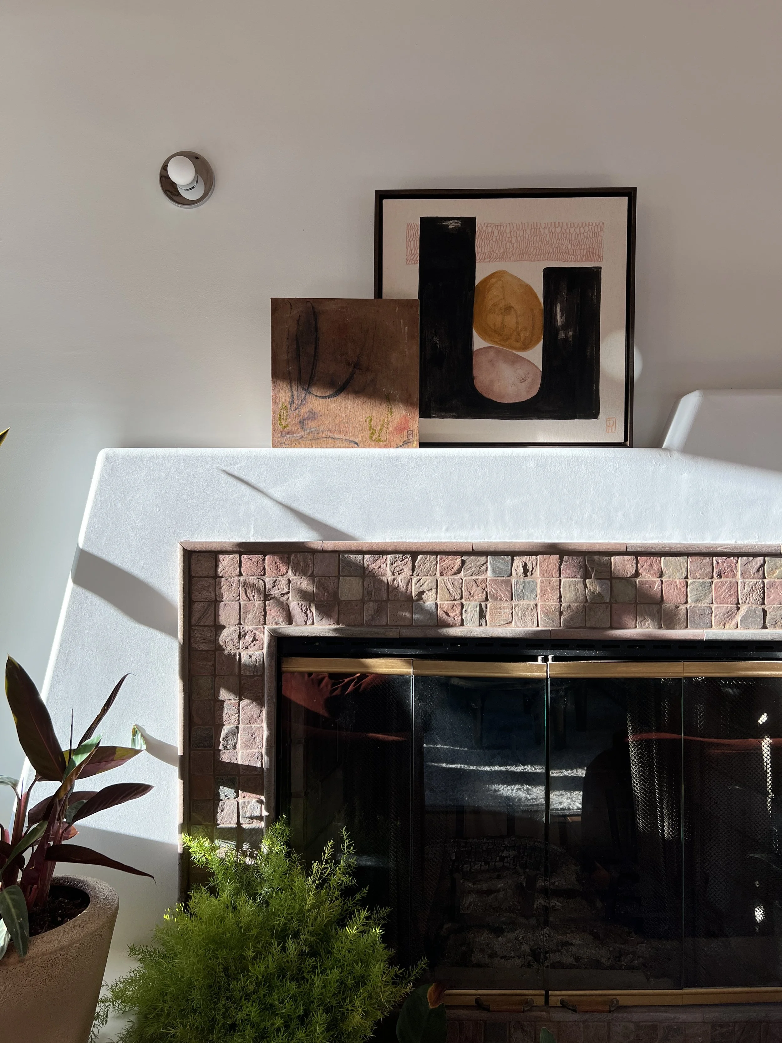 Fireplace with a white mantel, layered artwork, and plants.