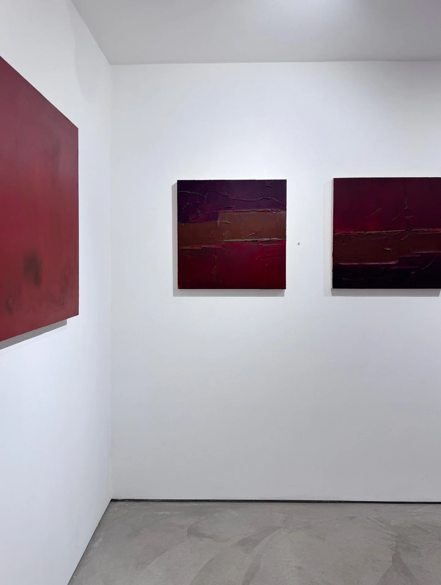 Red abstract paintings installed around a white gallery corner
