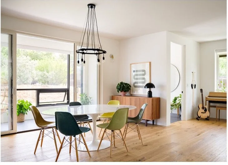 Dining table with colorful shell chairs beneath a black chandelier