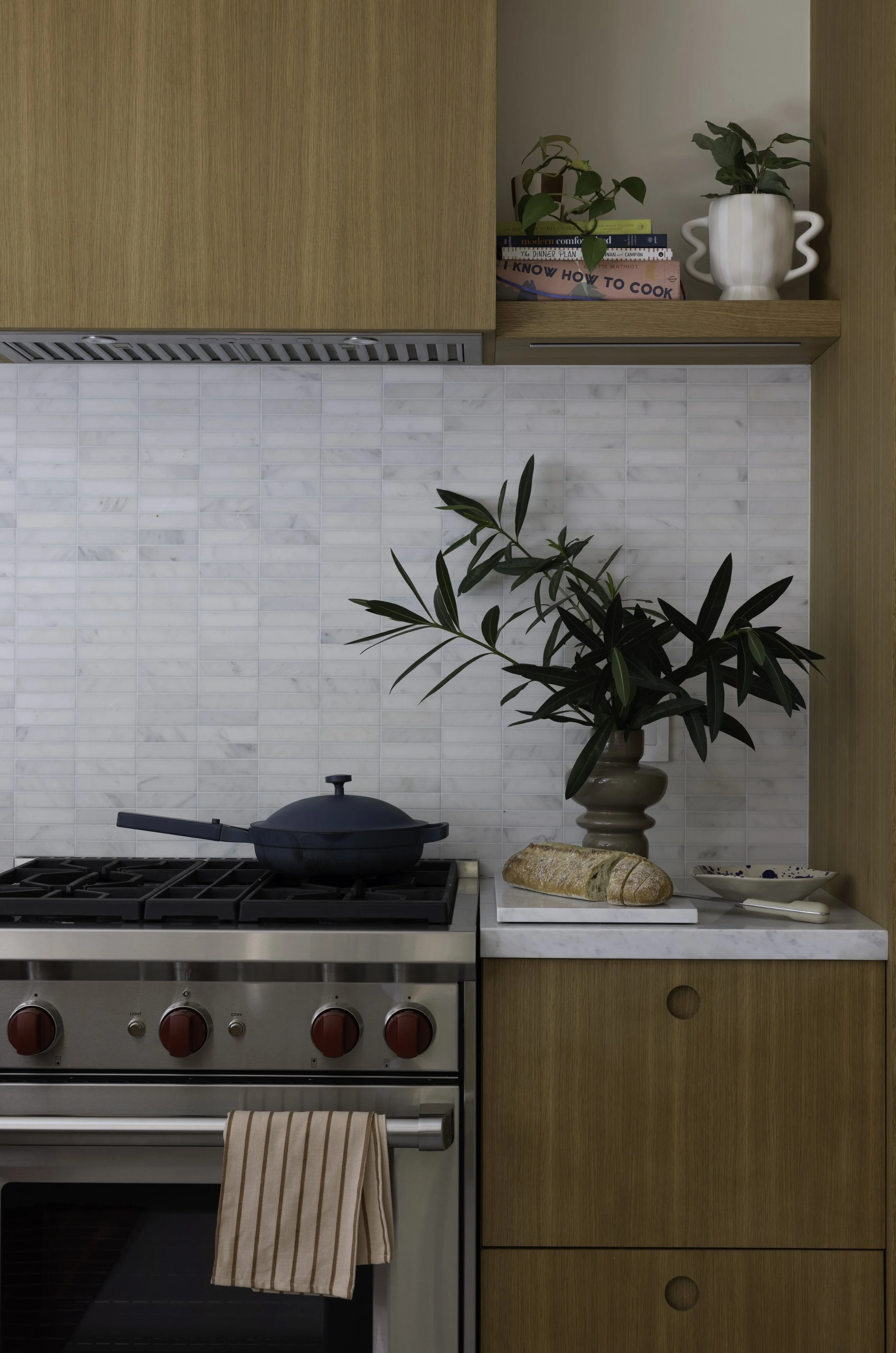 Kitchen range with wood cabinetry, a white tile backsplash, and plants.