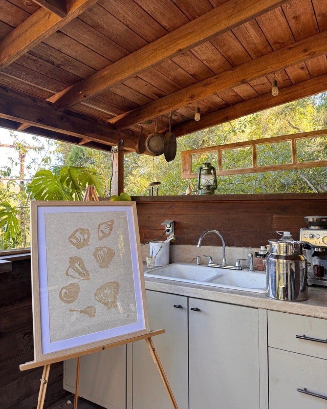 An outdoor kitchen under a wood roof with a framed art display