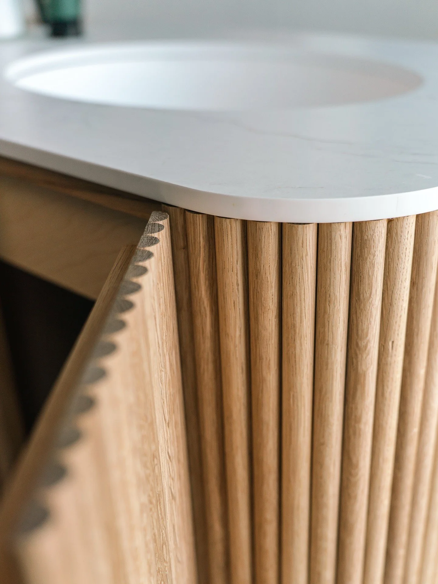 Close-up of curved fluted wood vanity beneath a white counter