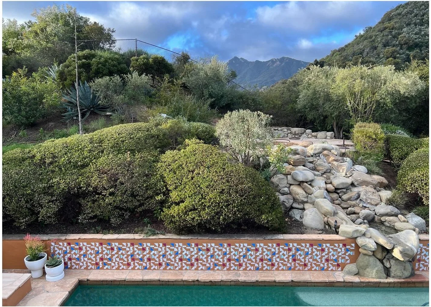 Pool beneath a rocky planted hillside and patterned tiled wall