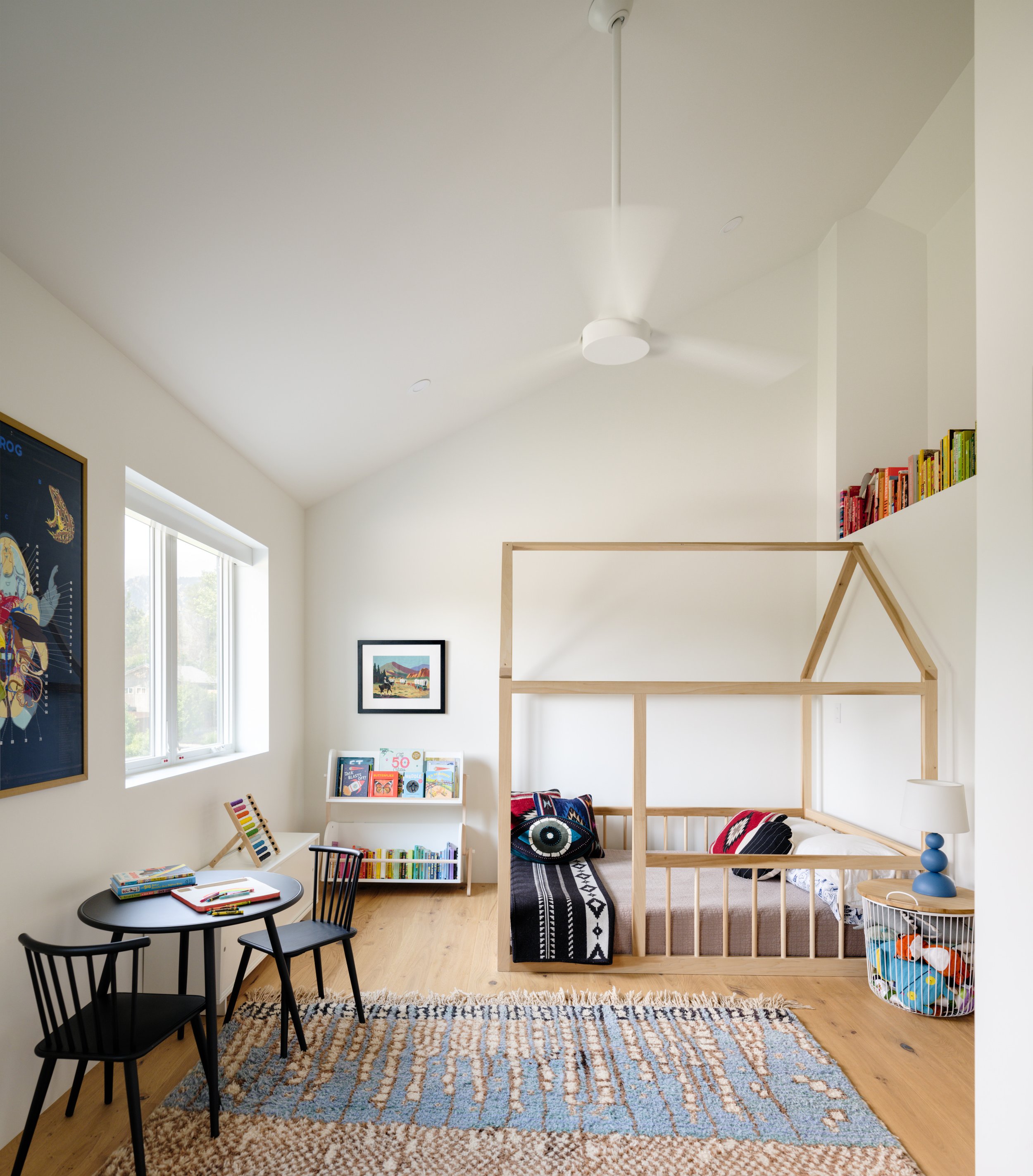 Bright child’s bedroom with a house-shaped bed frame, books, and a patterned rug.