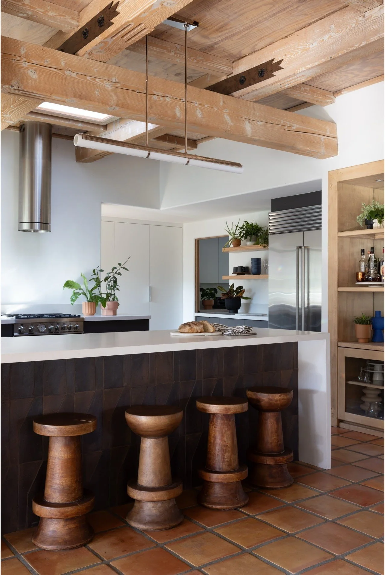 Kitchen island with wood stools and beams above terracotta floors